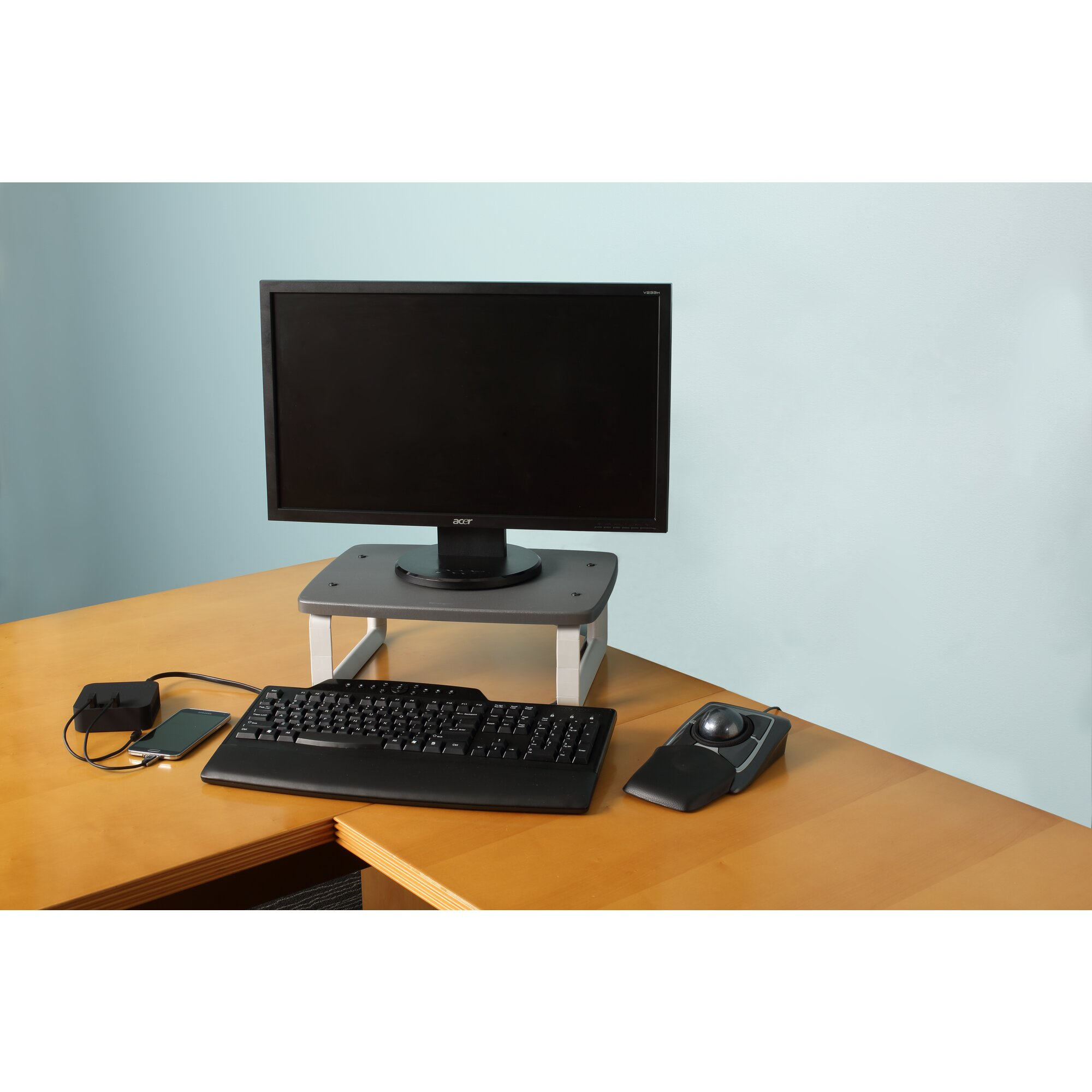 Ein Computer-Setup mit Monitor, Tastatur, Maus und Telefon auf einem Holzschreibtisch. Eine blaue Wand ist der Hintergrund.