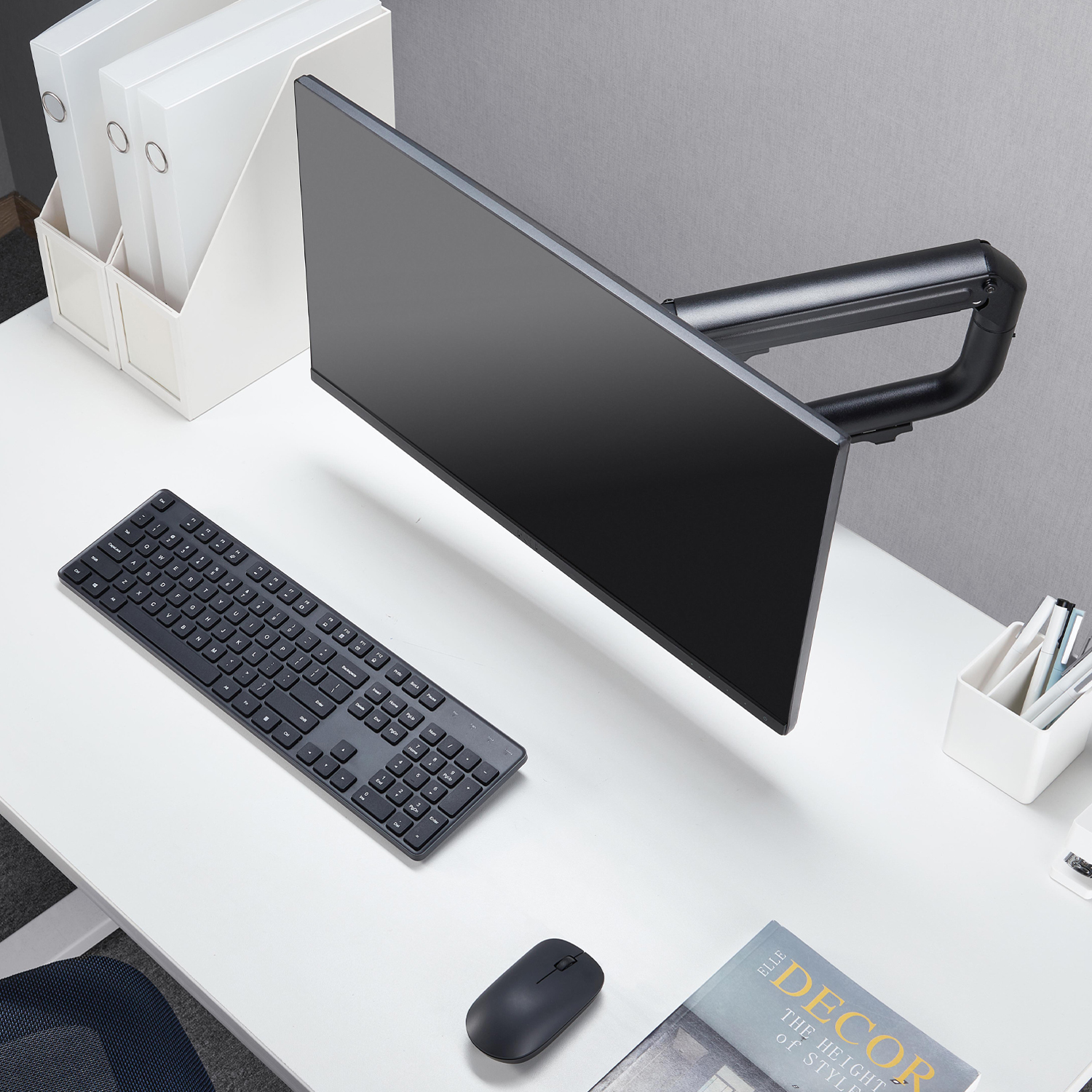 Konfiguracja komputera z monitorem, klawiaturą, myszą i artykułami biurowymi na białym biurku. Obecny jest również magazyn.