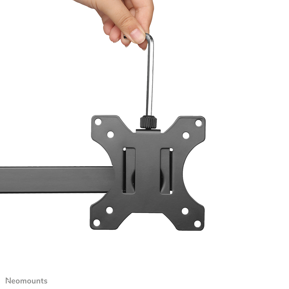 Hand hält ein Metallwerkzeug über einer schwarzen Metallhalterung. Die Halterung hat Löcher und Schlitze, Teil einer Monitorhalterung.