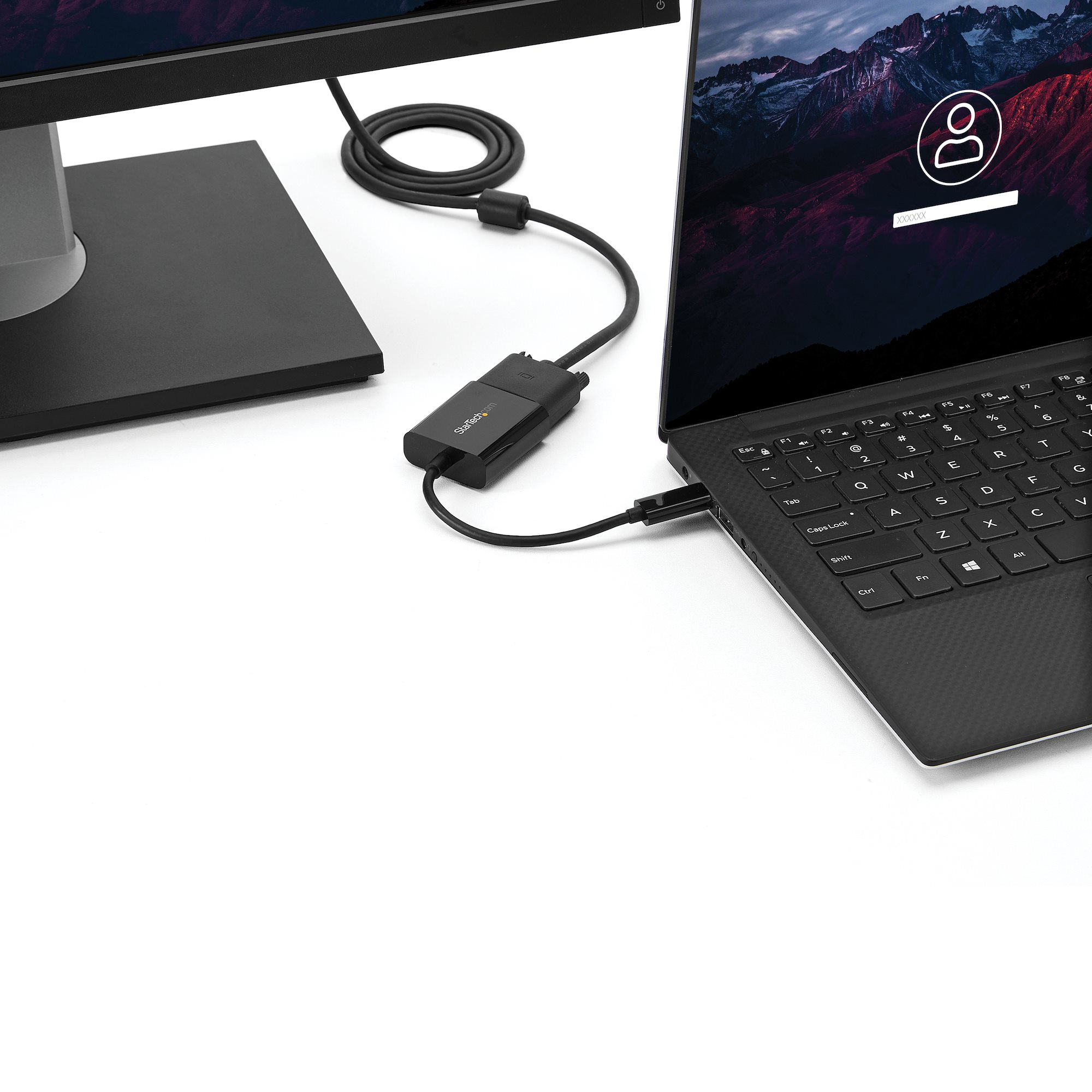 Laptop über einen Adapter mit einem Monitor verbunden. Der Laptop-Bildschirm zeigt einen Anmeldebildschirm mit Bergen.