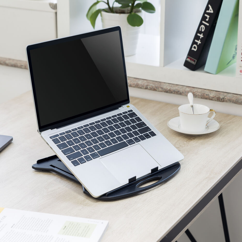 Laptop auf schwarzem Ständer, Kaffeetasse, Bücher und Pflanze auf einem Holztisch. Der Laptop-Bildschirm ist schwarz.