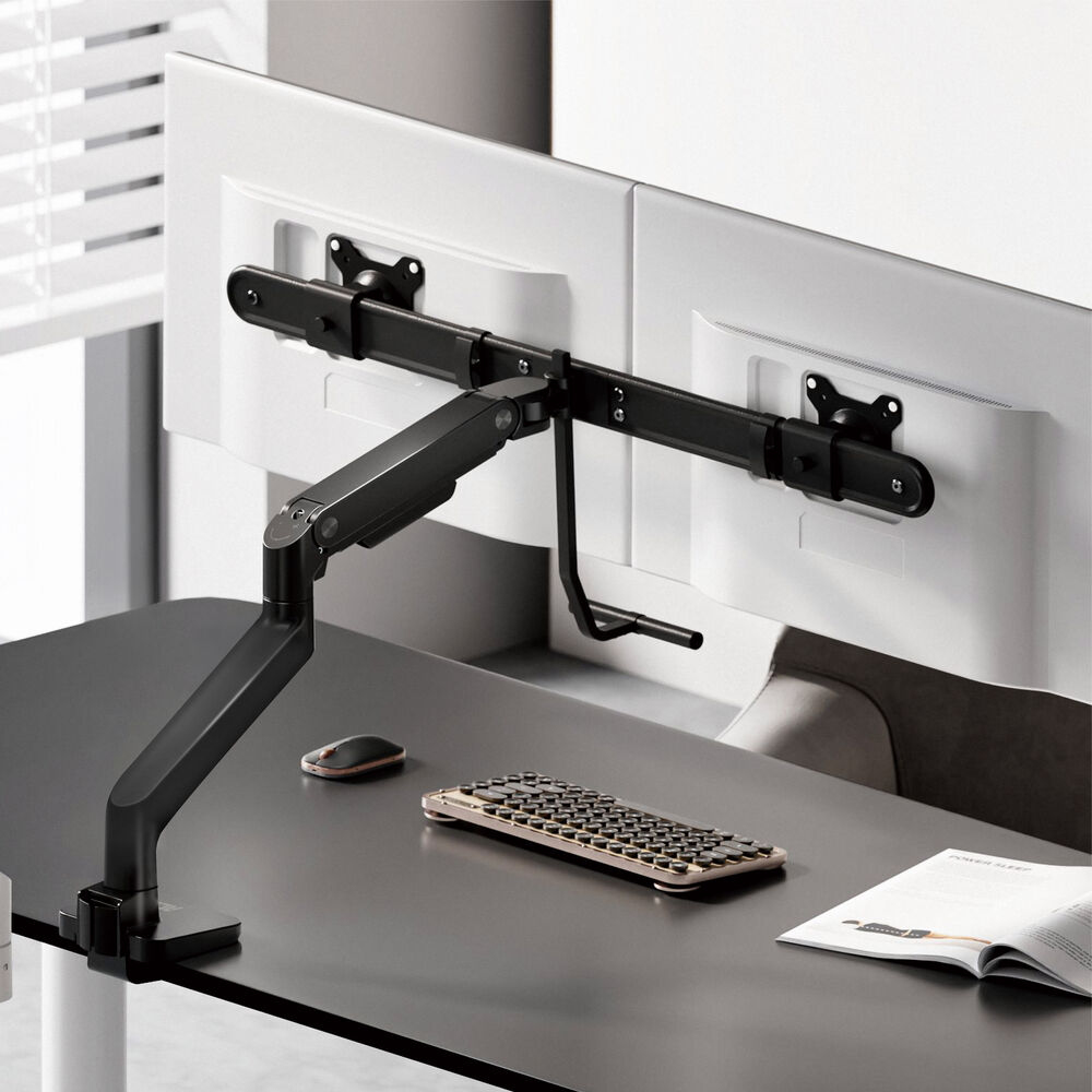 Een bureau-opstelling met twee monitoren, een toetsenbord en een muis. Een zwarte monitorarm houdt de monitoren vast. Er ligt een boek op het bureau.