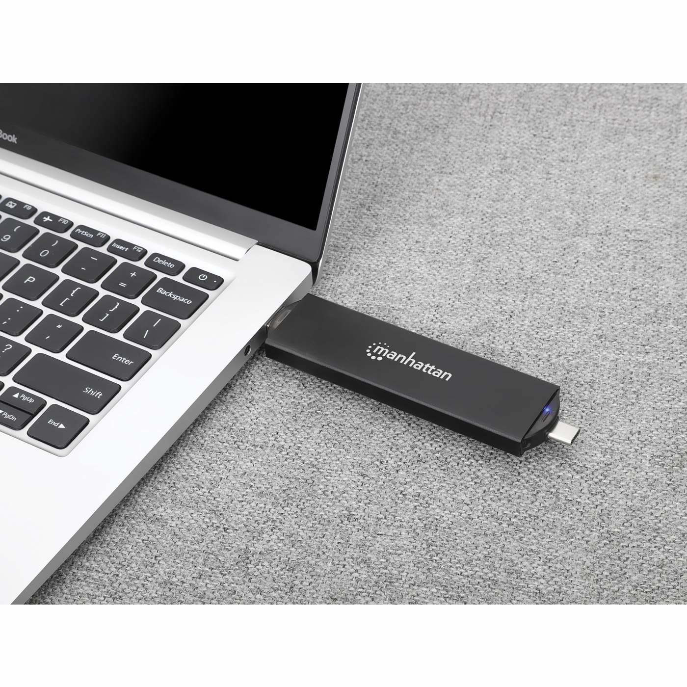 Ein Laptop mit einem schwarzen USB-Laufwerk. Das Laptop steht auf einer grauen Oberfläche. Auf dem USB-Laufwerk steht "manhattan".