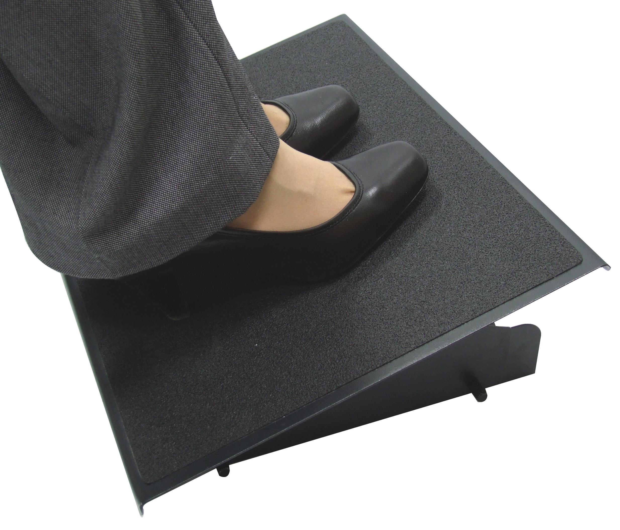 A person's feet in black shoes on a black footrest. Dark pants are visible.