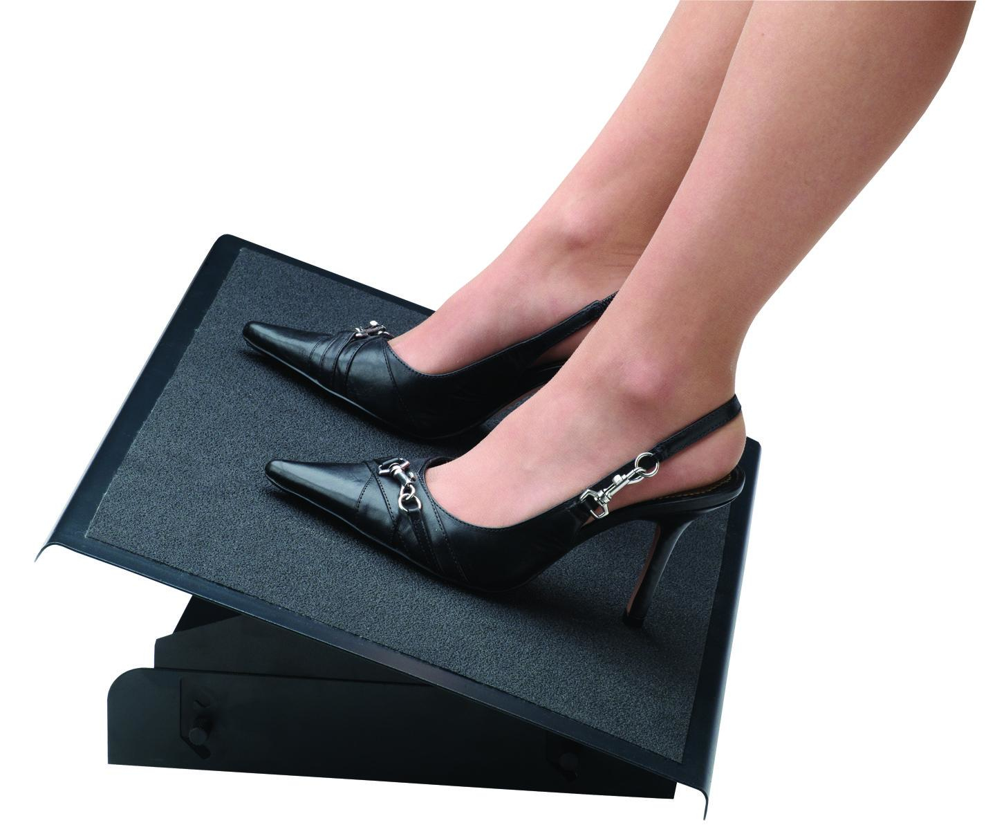 Woman's legs with black high heels on a footrest. The shoes have straps and silver buckles. The footrest is black.
