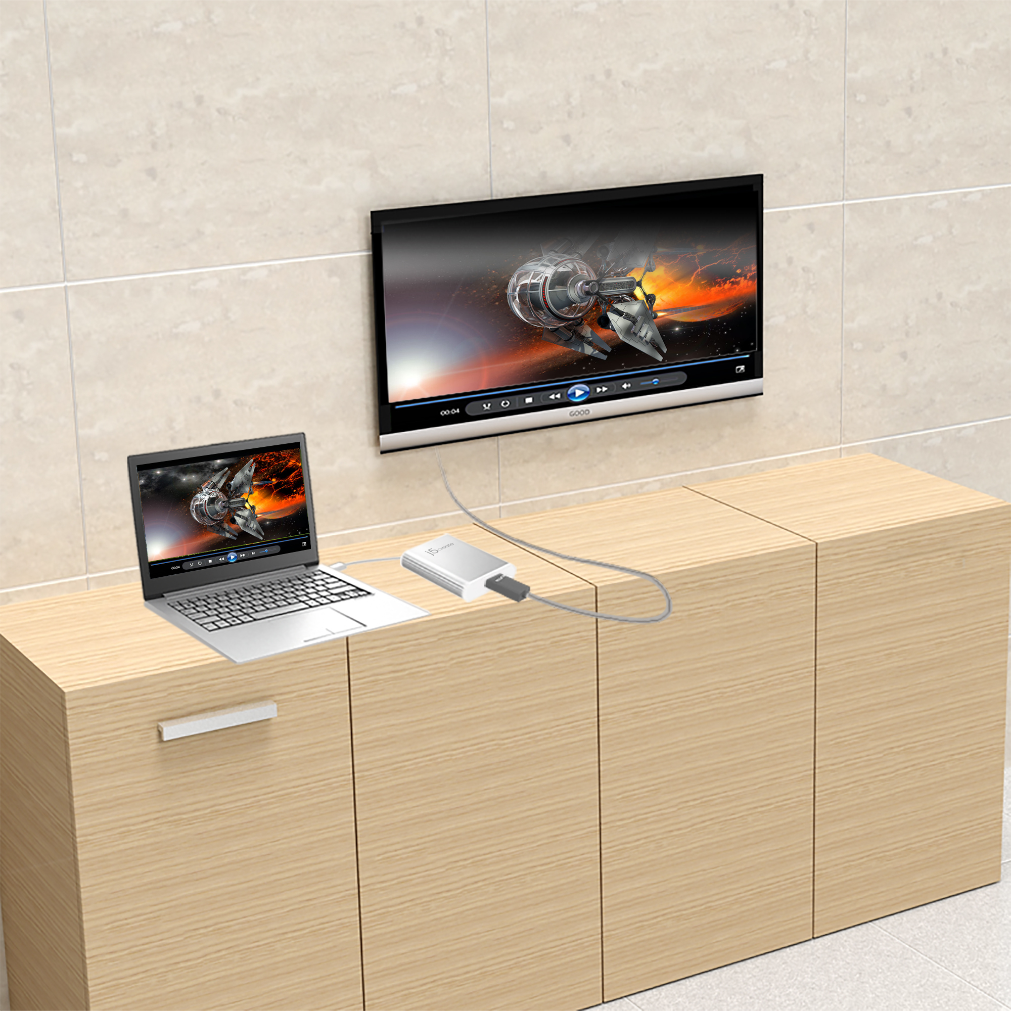 Una laptop y un televisor muestran un video de nave espacial. Están conectados por un cable. El televisor cuelga sobre un mueble de madera.