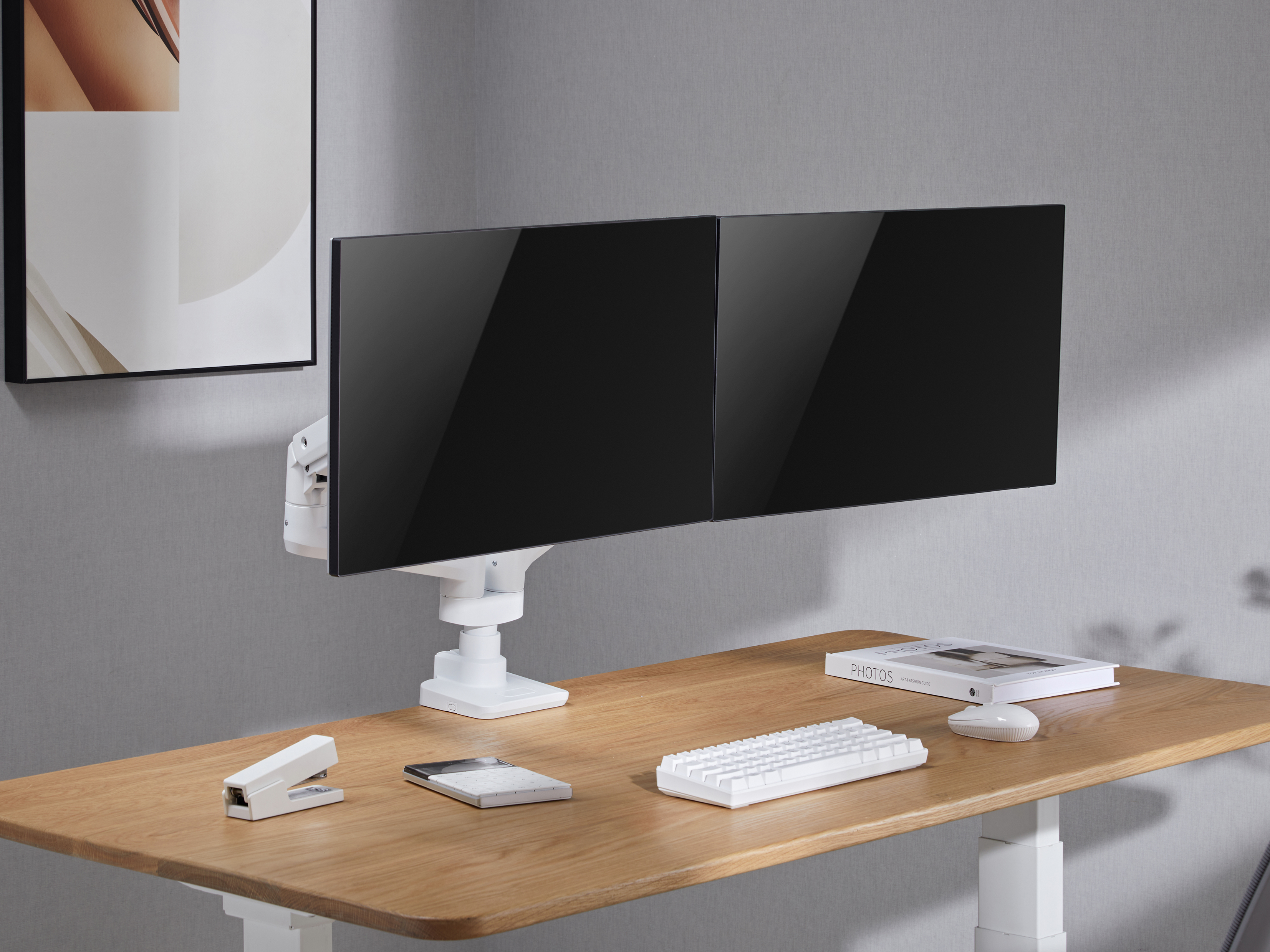Een bureau met twee zwarte monitoren, een toetsenbord, een muis, een nietmachine, een rekenmachine en een boek.