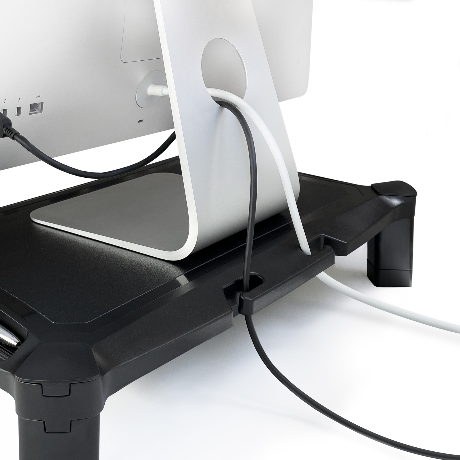 Un monitor de computadora se encuentra sobre un soporte negro. Los cables, negro y blanco, están conectados al monitor y pasan por el soporte.