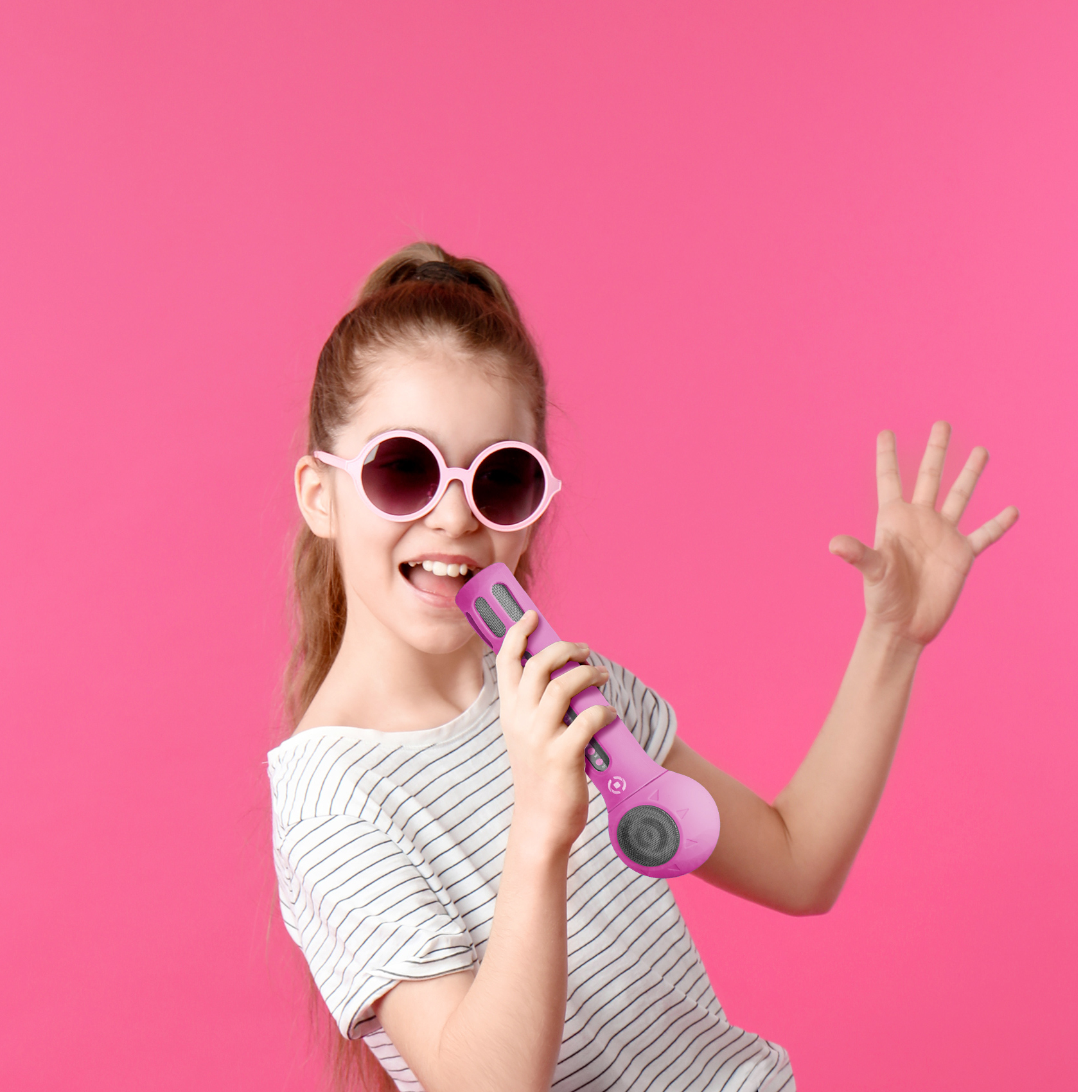 Ein Mädchen mit Sonnenbrille singt in ein pinkes Mikrofon und hebt eine Hand. Pinker Hintergrund.