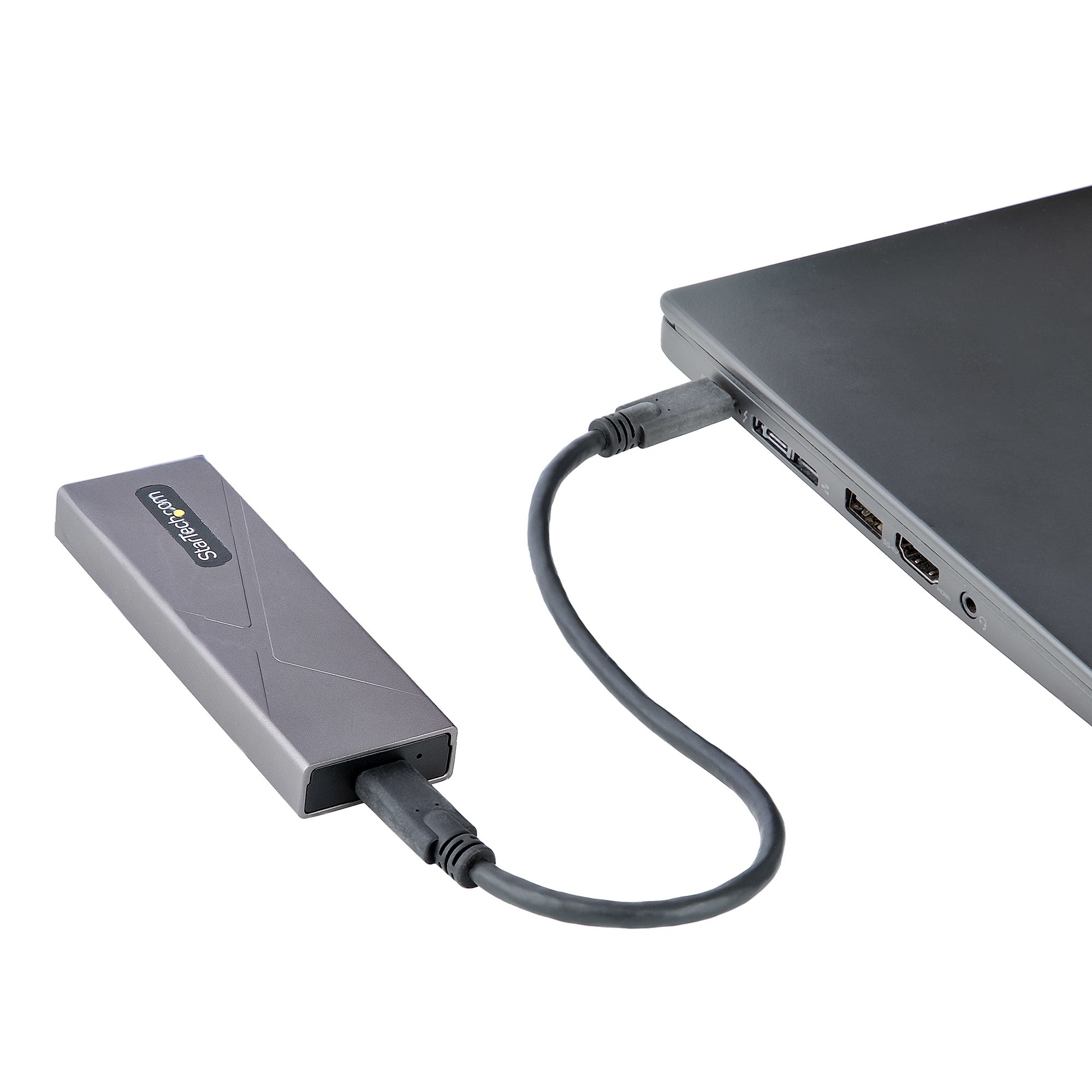 Un disco rigido esterno grigio è collegato a un laptop tramite un cavo USB-C. Il laptop è su una superficie bianca.