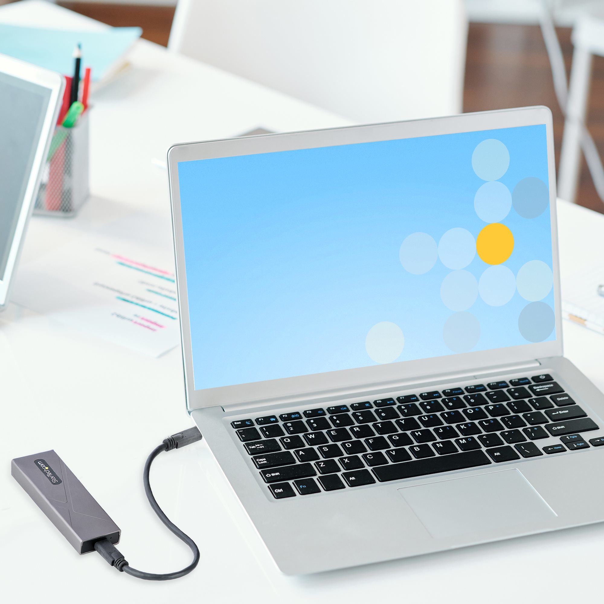 Laptop con schermo blu con cerchi, collegato a un disco rigido esterno. Il laptop è su una scrivania bianca.