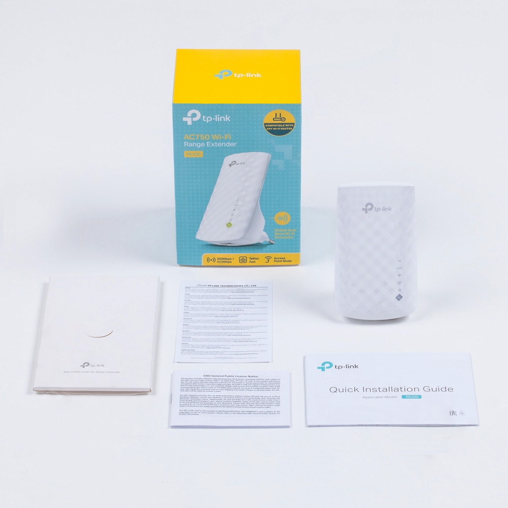 Ein weißer TP-Link WLAN-Repeater, Schachtel und Handbücher liegen auf einer weißen Oberfläche. Auf der Schachtel steht AC750 Wi-Fi Range Extender.
