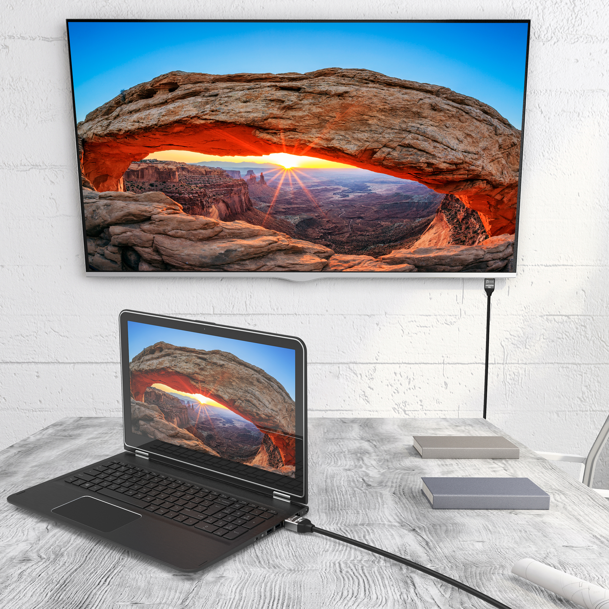 Laptop und Fernseher zeigen einen malerischen Bogen. HDMI-Kabel verbindet sie. Bücher liegen auf dem Holztisch. Weiße Wand im Hintergrund.