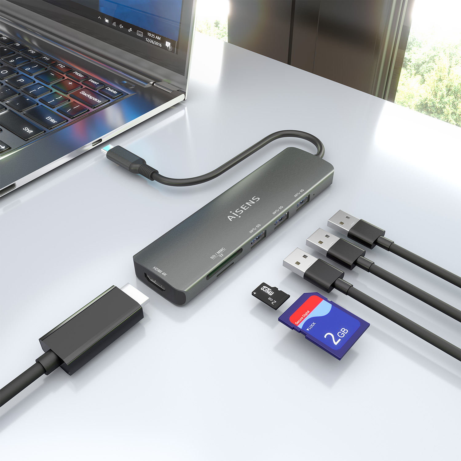 Un laptop con un hub USB, schede SD e cavi USB su una superficie bianca. L'hub è collegato al laptop e ha più porte.