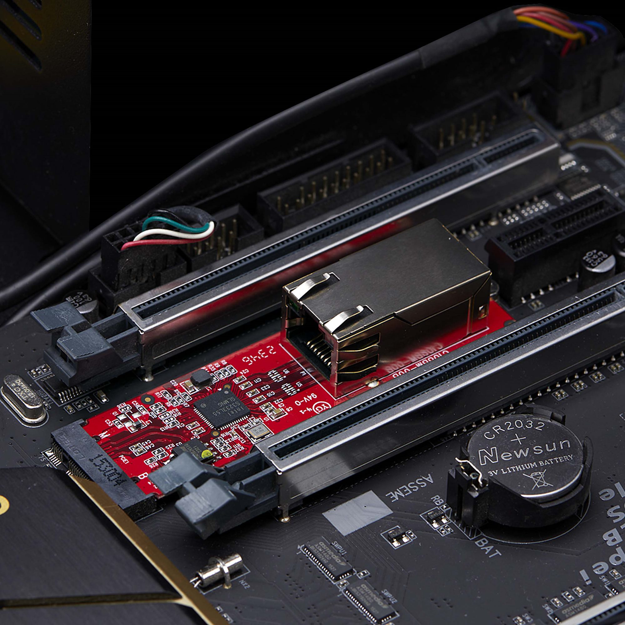 Nahaufnahme eines Computer-Motherboards mit einer roten Erweiterungskarte, einer Batterie und verschiedenen Anschlüssen.