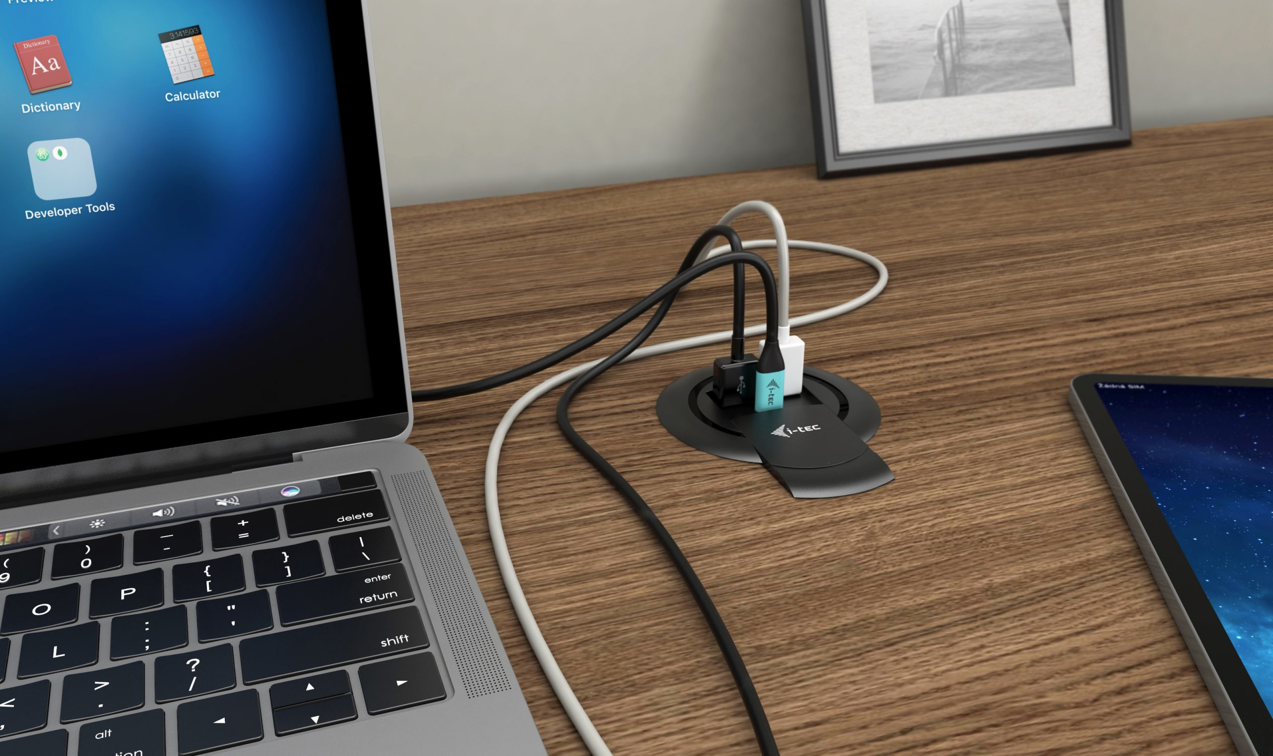 Un ordinateur portable, des câbles et une tablette sont sur un bureau en bois. Un hub d'alimentation avec des câbles au centre. Cadre photo à droite.