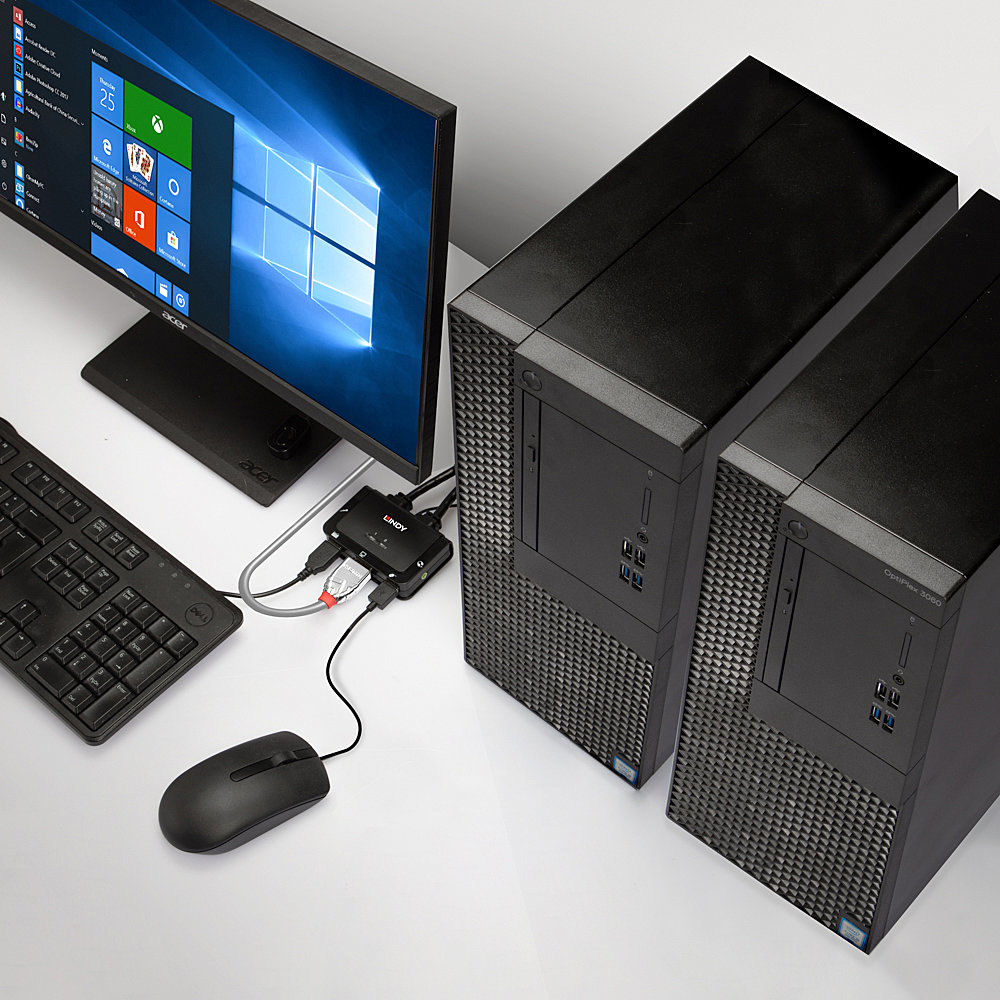 Una configuración de computadora con monitor, teclado, ratón y dos torres de escritorio negras. Un interruptor LINDY está conectado.