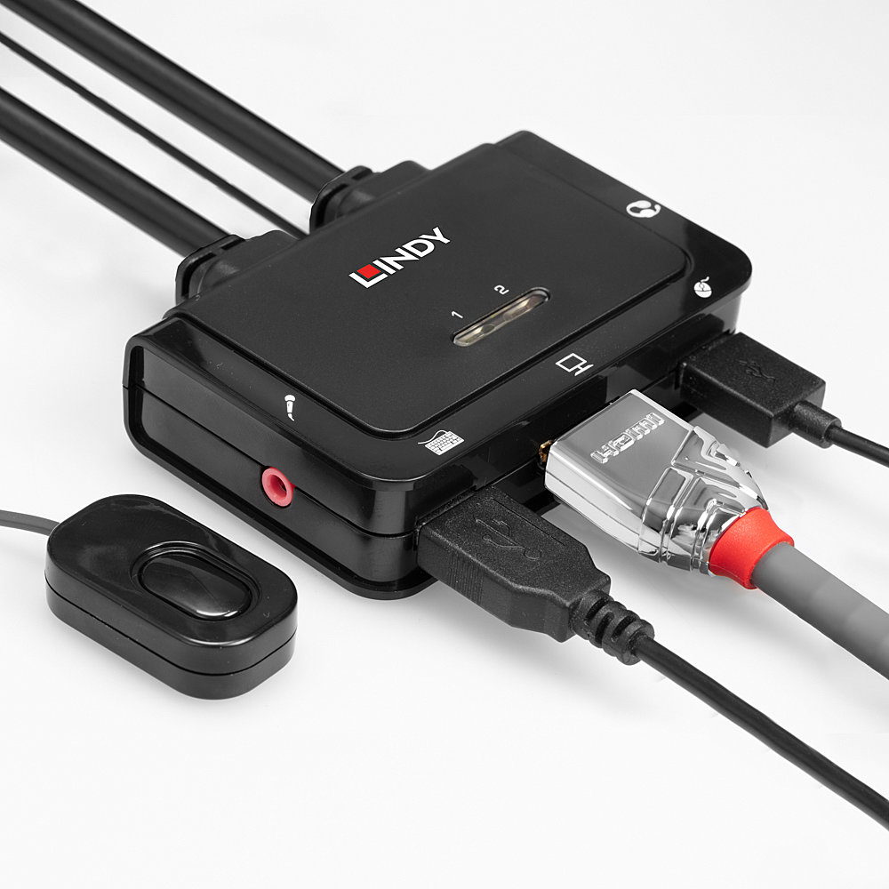 Un dispositivo LINDY negro con múltiples puertos y cables. Incluye un cable HDMI, un cable USB y un mando a distancia. El fondo es blanco.