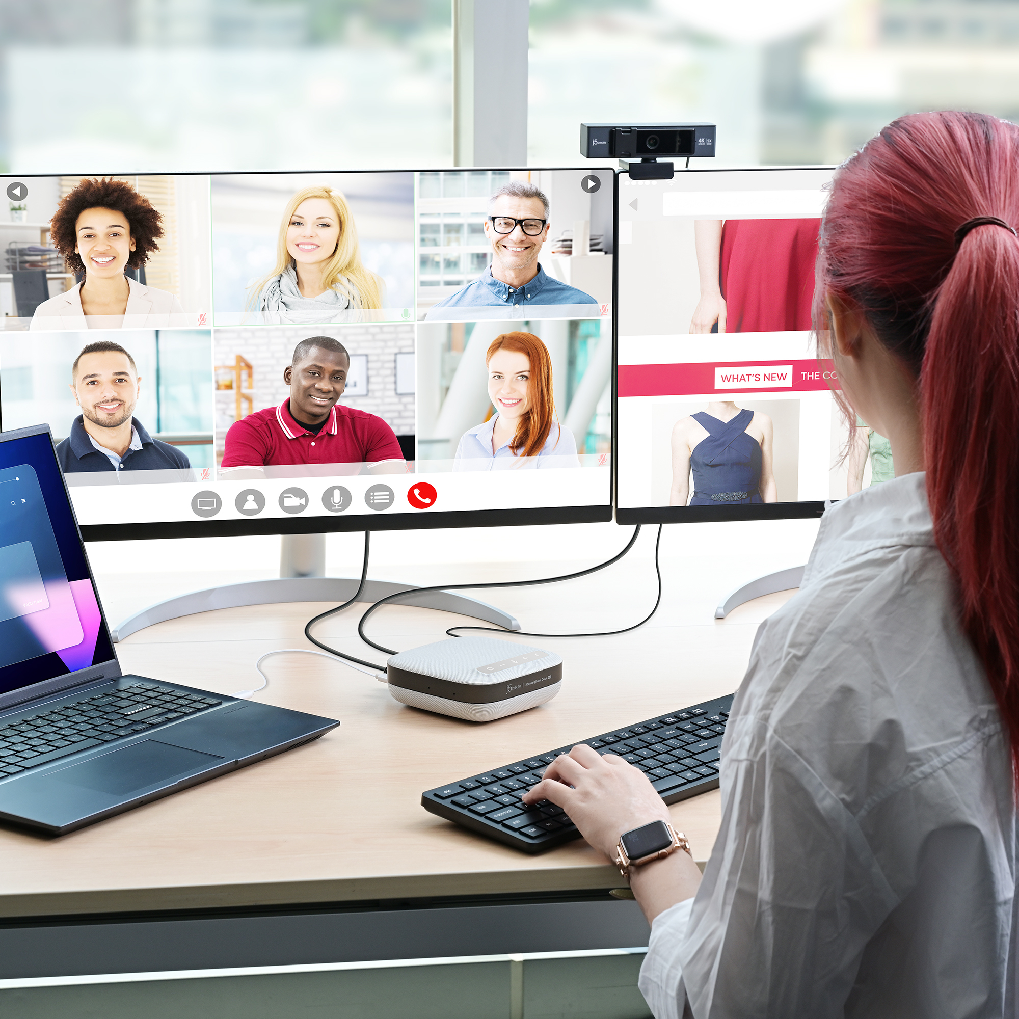 Eine Frau mit roten Haaren arbeitet an einem Computer. Der Bildschirm zeigt einen Videoanruf und eine Website.
