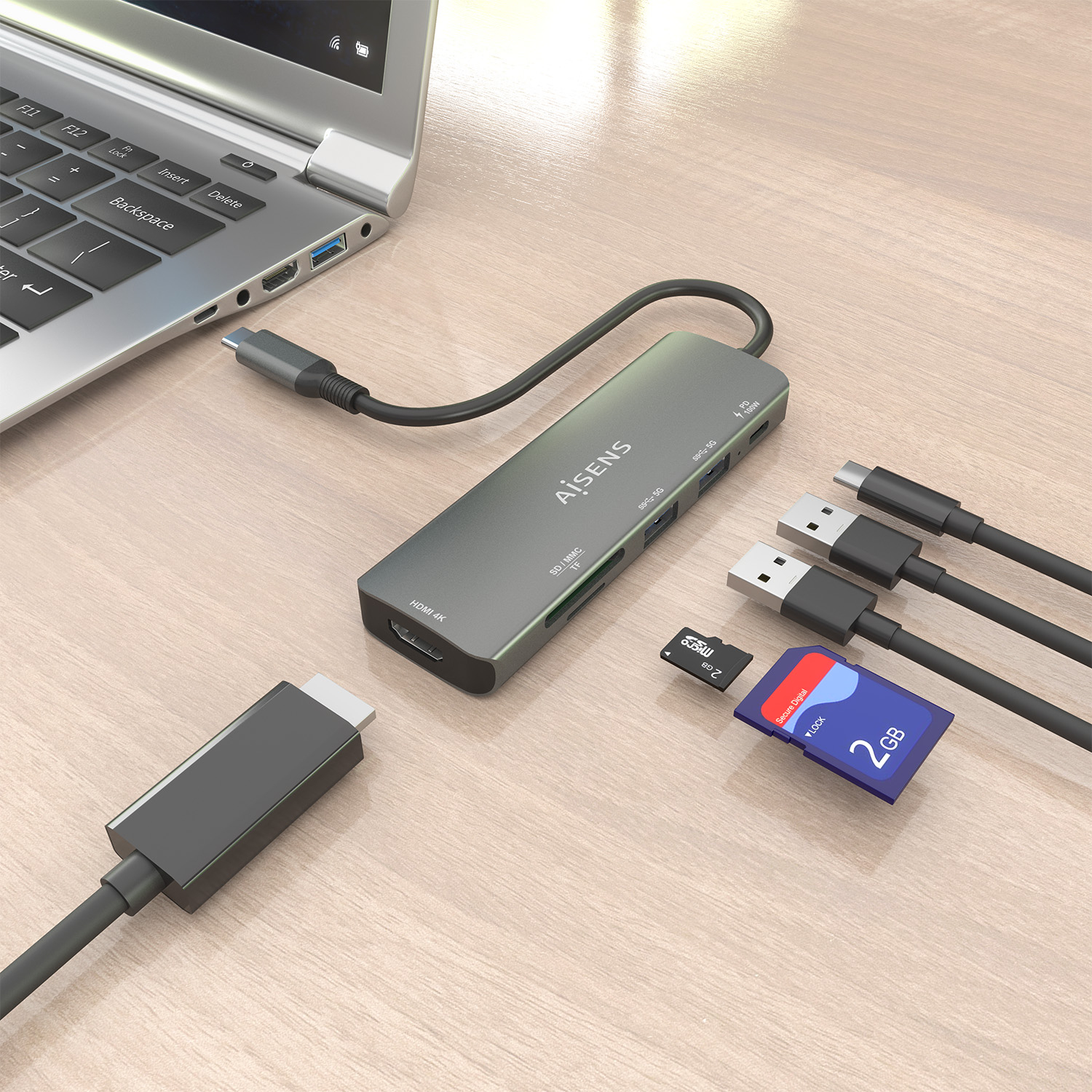 Laptop con hub USB, scheda SD e cavi USB su una superficie di legno. L'hub ha slot HDMI, USB e per schede. Le schede leggono 2 GB.