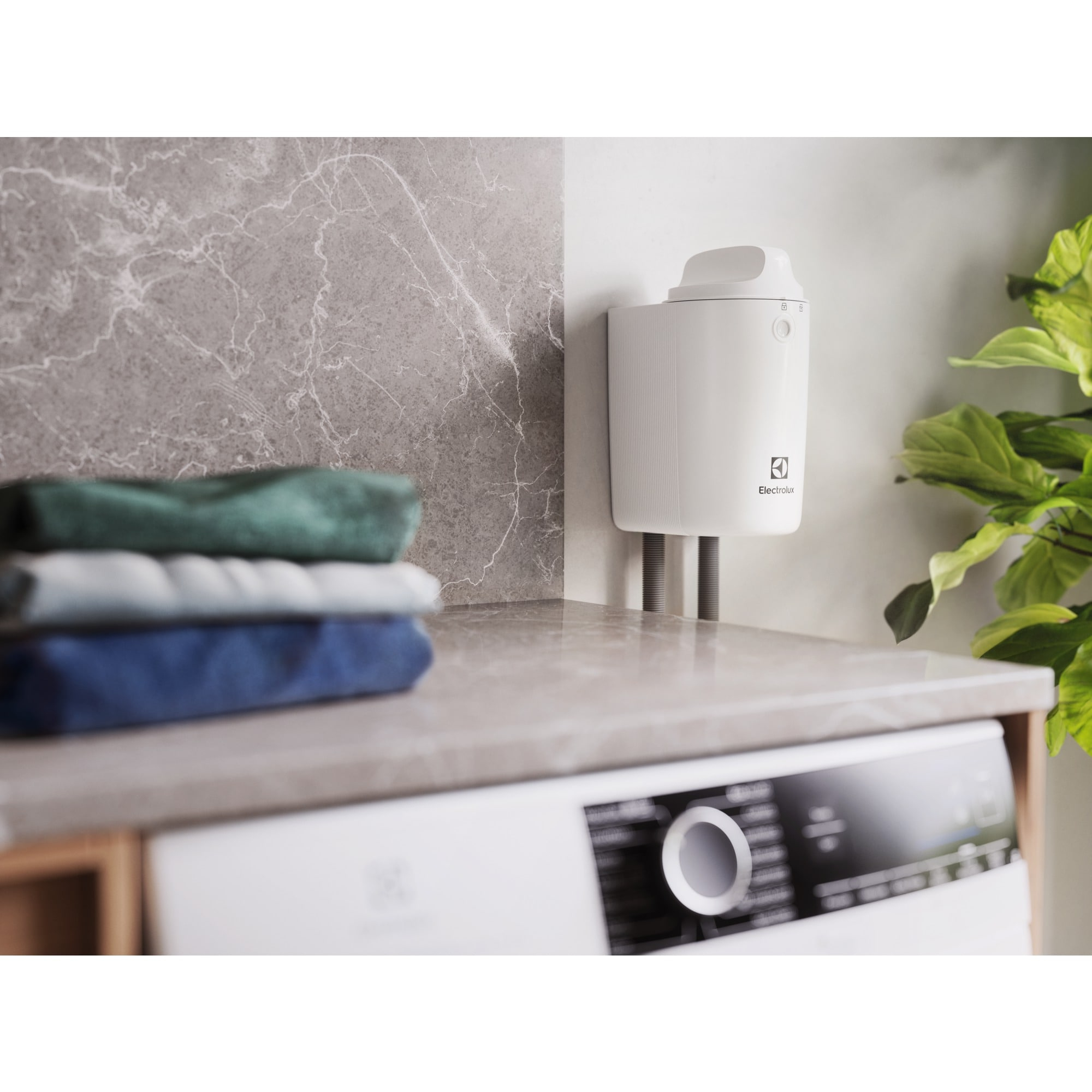 Ein weißes Electrolux-Waschgerät steht auf einer Arbeitsplatte. Gestapelte Handtücher befinden sich links. Rechts ist eine Pflanze.