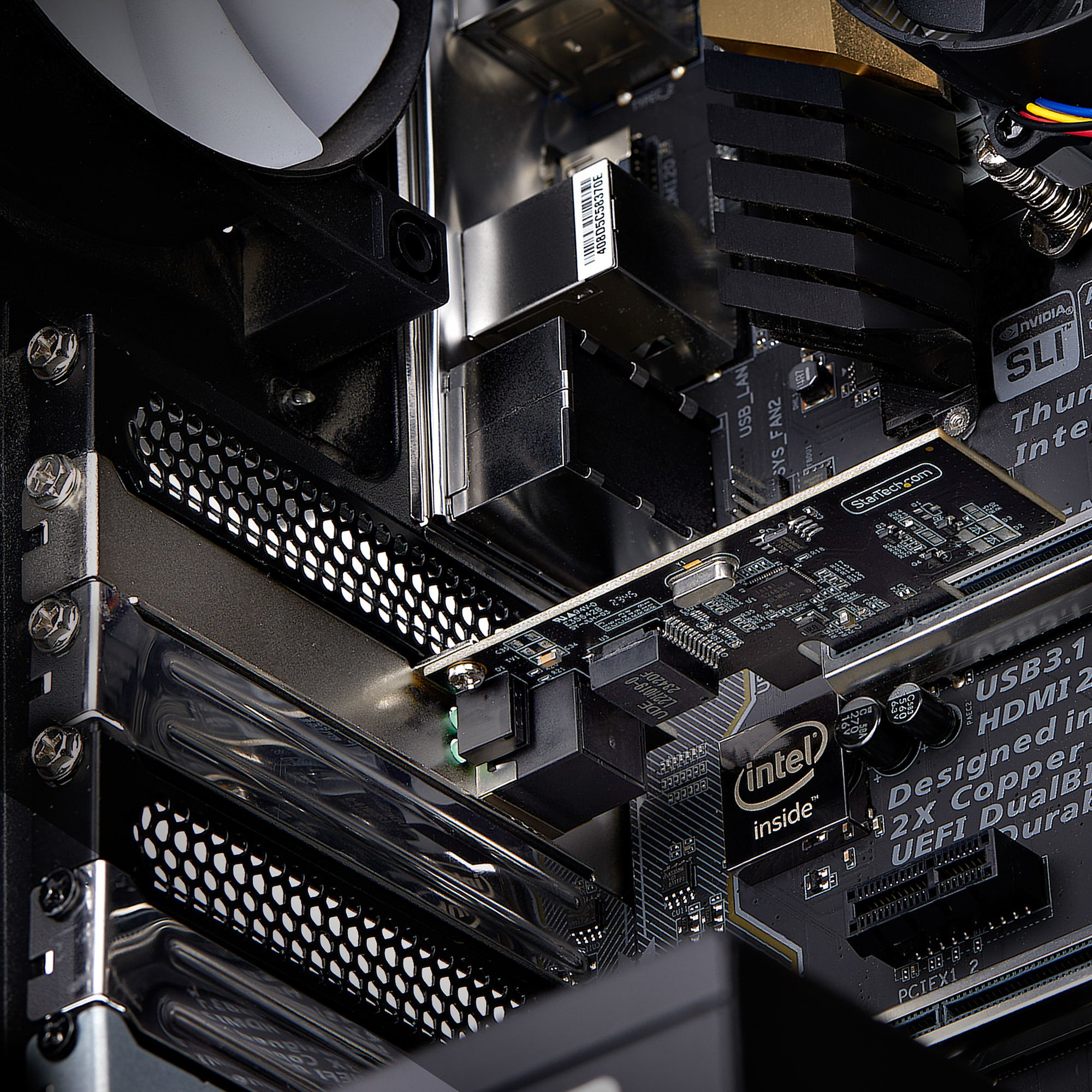 Nahaufnahme des Inneren eines Computers. Eine schwarze Leiterplatte mit integrierten Komponenten, ein Lüfter und metallische Komponenten.