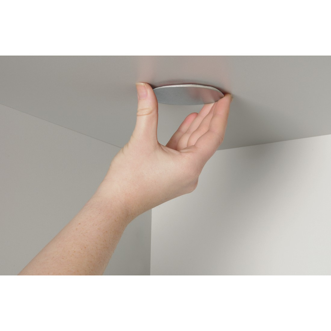 Eine Hand hält eine silberne Scheibe gegen eine weiße Oberfläche, möglicherweise eine Decke. Die Hand ist hell, der Hintergrund ist einfach.