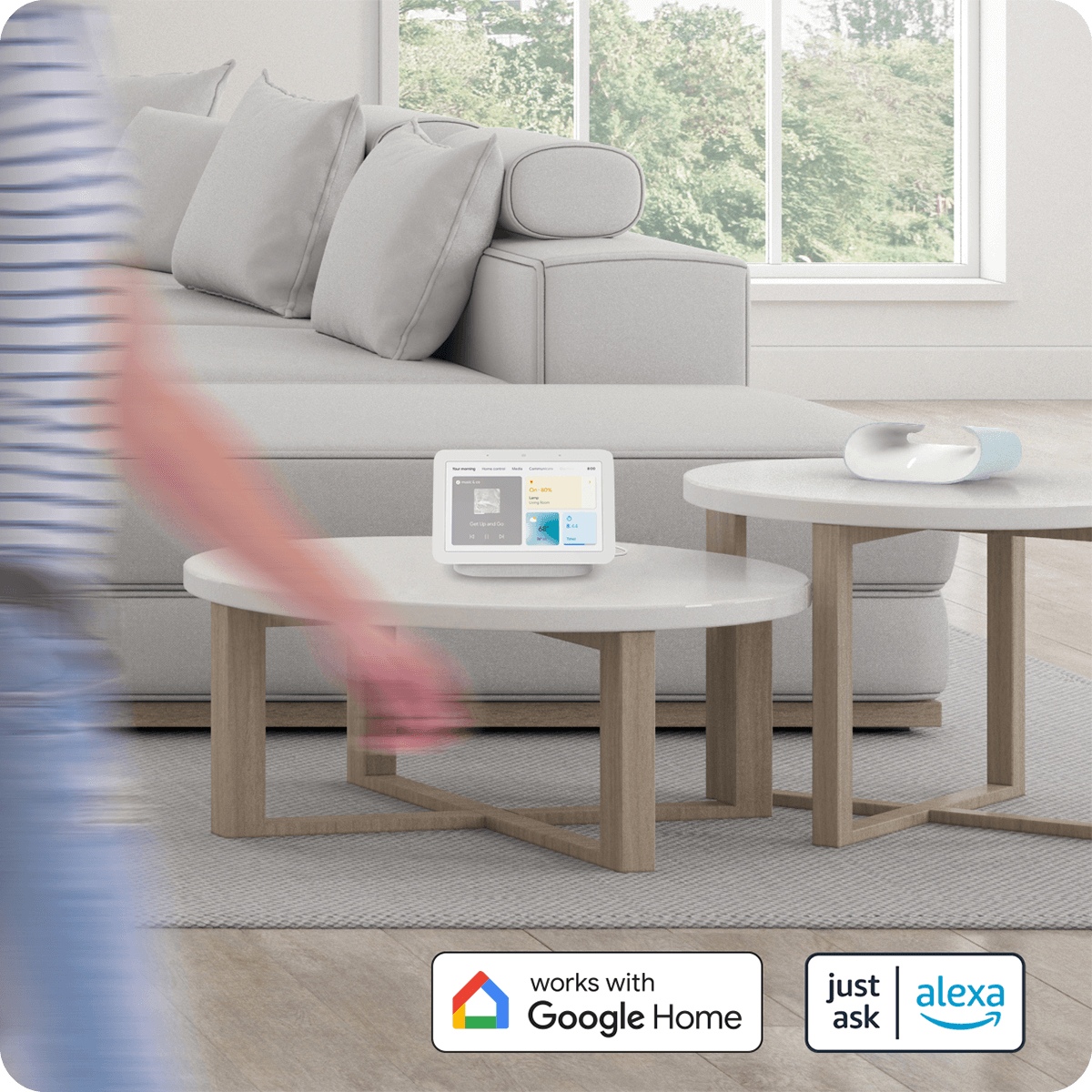 Nowoczesny salon z inteligentnym wyświetlaczem na stole. Osoba jest rozmyta w ruchu. Logo Google Home i Alexa.