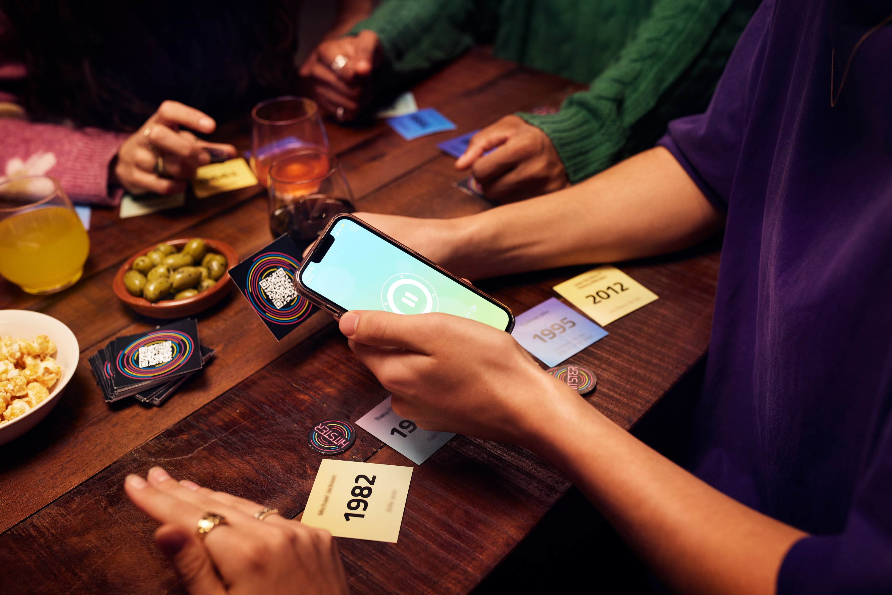 Ludzie grają w karty na drewnianym stole. Telefon z przyciskiem pauzy jest trzymany.