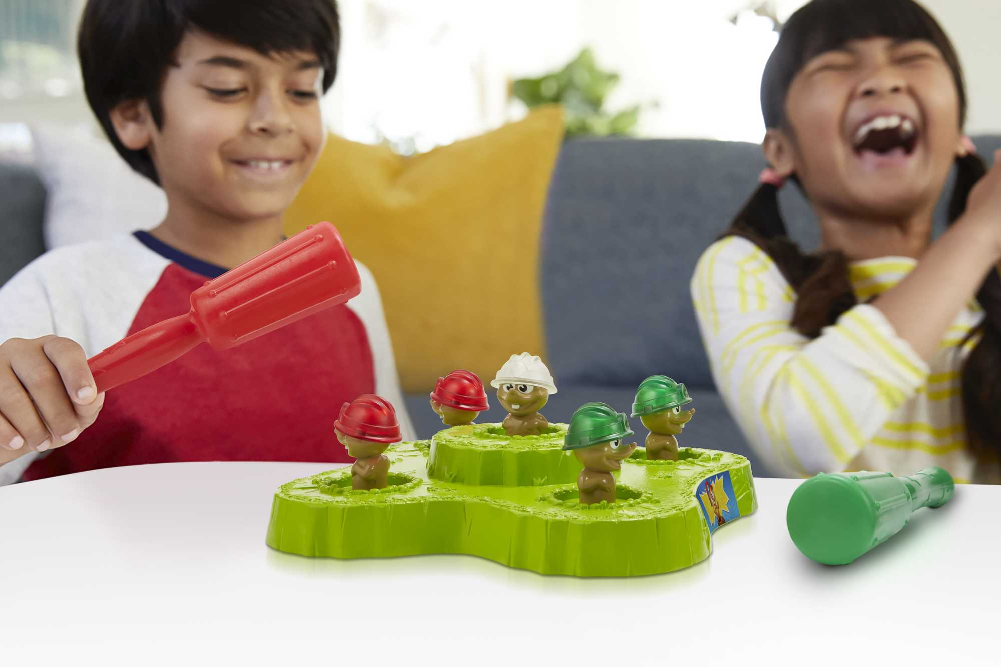 Due bambini giocano a un gioco di colpire le talpe. Uno tiene in mano un martello rosso, l'altro ride. Il gioco ha talpe con elmetti.