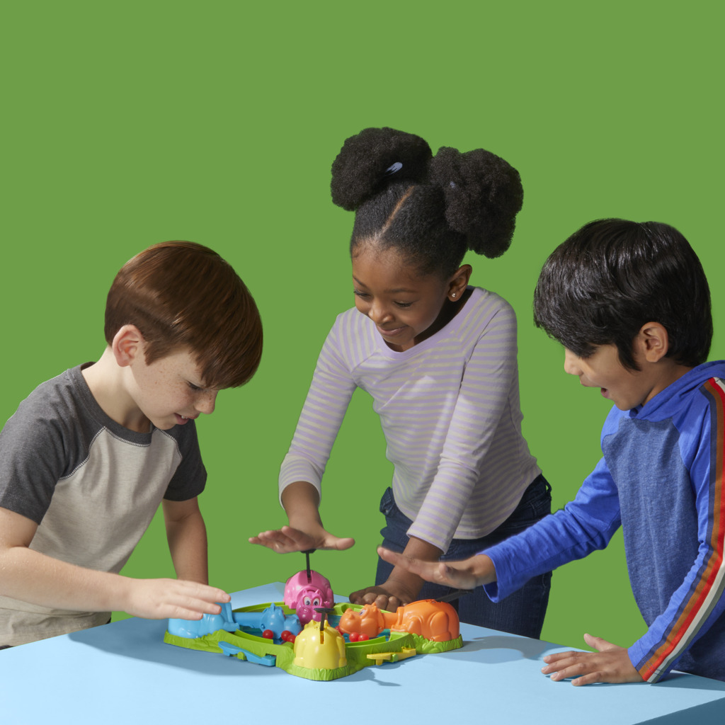 Tre bambini giocano con ippopotami di plastica su un tavolo azzurro, con sfondo verde.