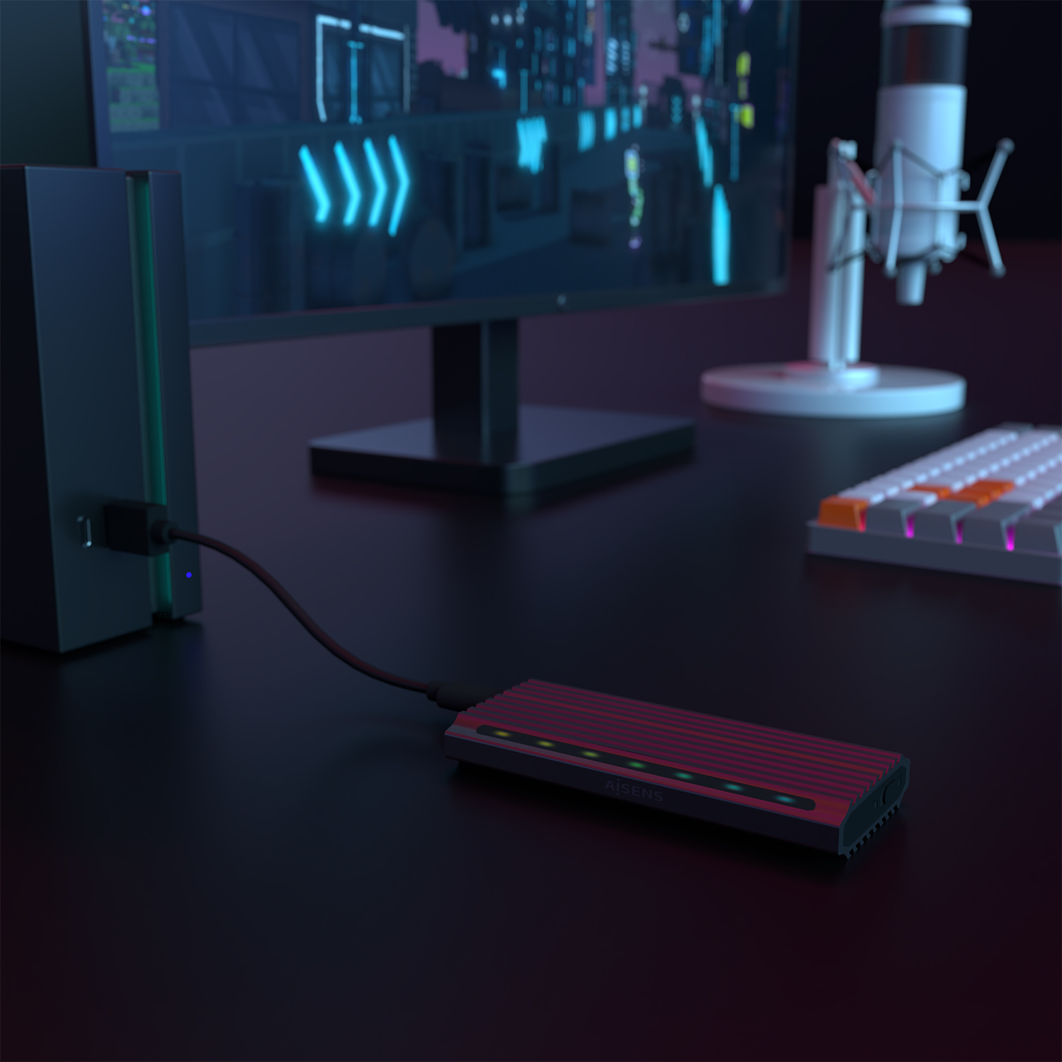 Un disco duro externo rojo con luces verdes está conectado a una computadora. Un teclado, un monitor y un micrófono están en un escritorio.