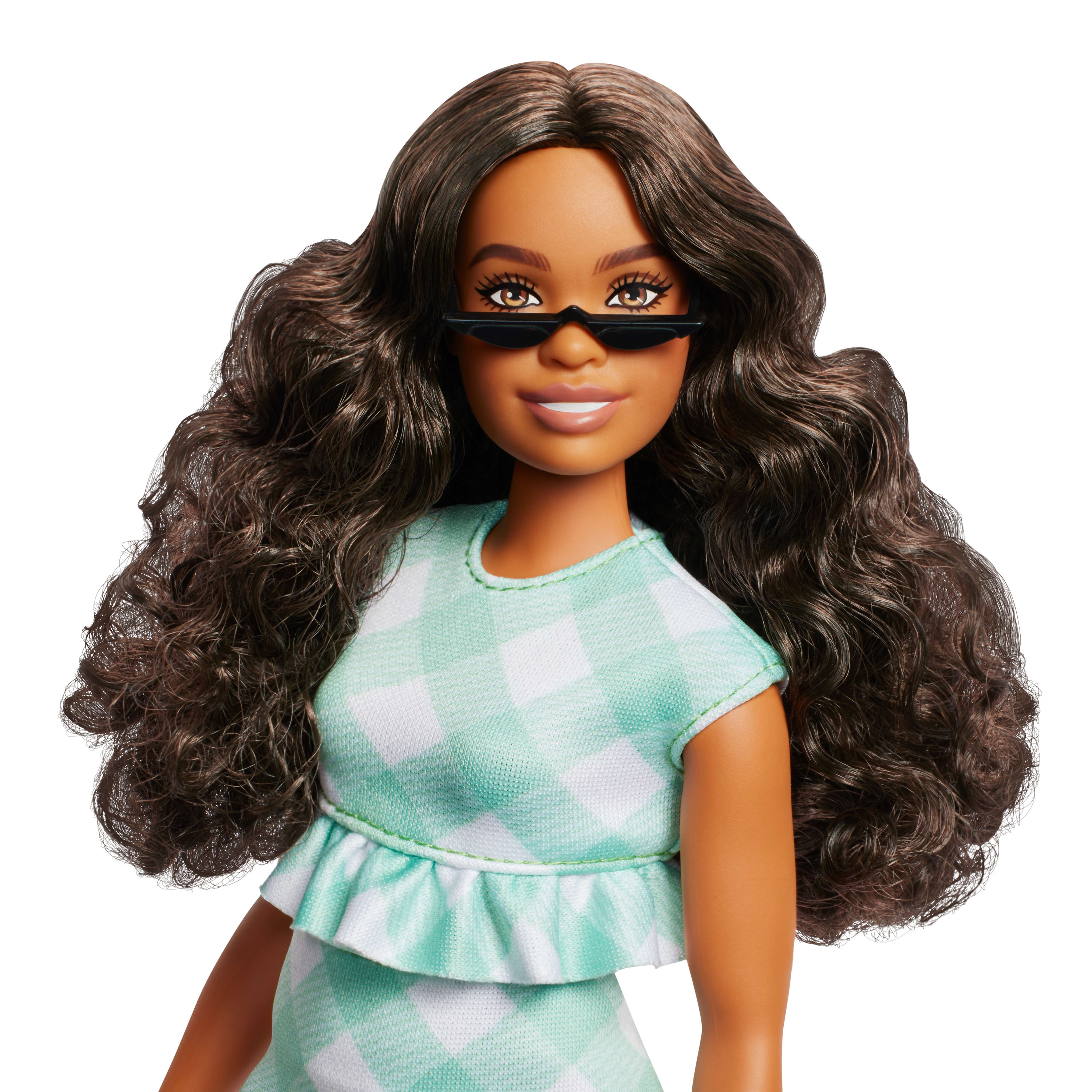 Eine Puppe mit dunkler Haut, Sonnenbrille und einem grün karierten Kleid. Lange, wellige braune Haare.