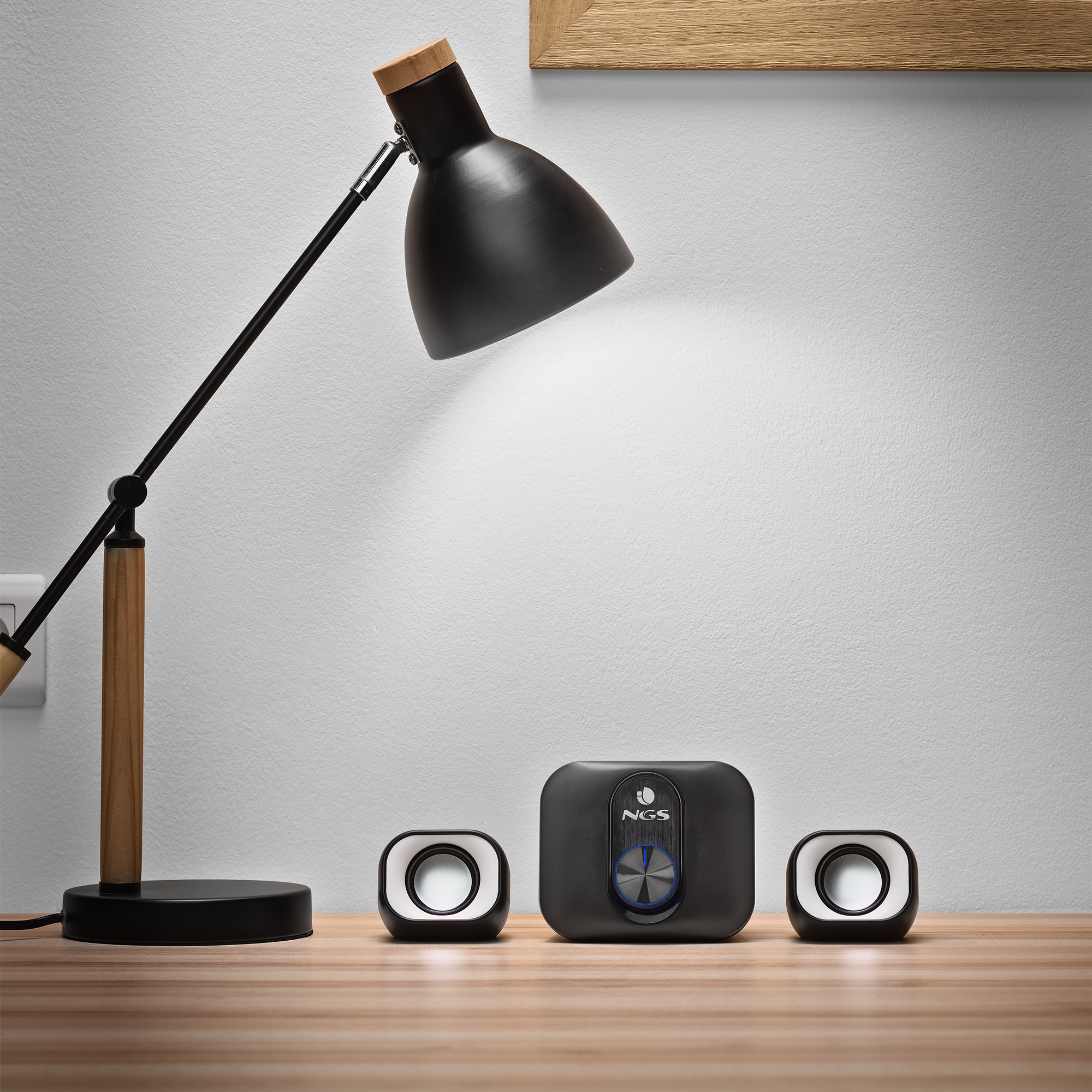 Una lámpara de escritorio y altavoces sobre una mesa de madera. Una pared con marco de madera en el fondo.