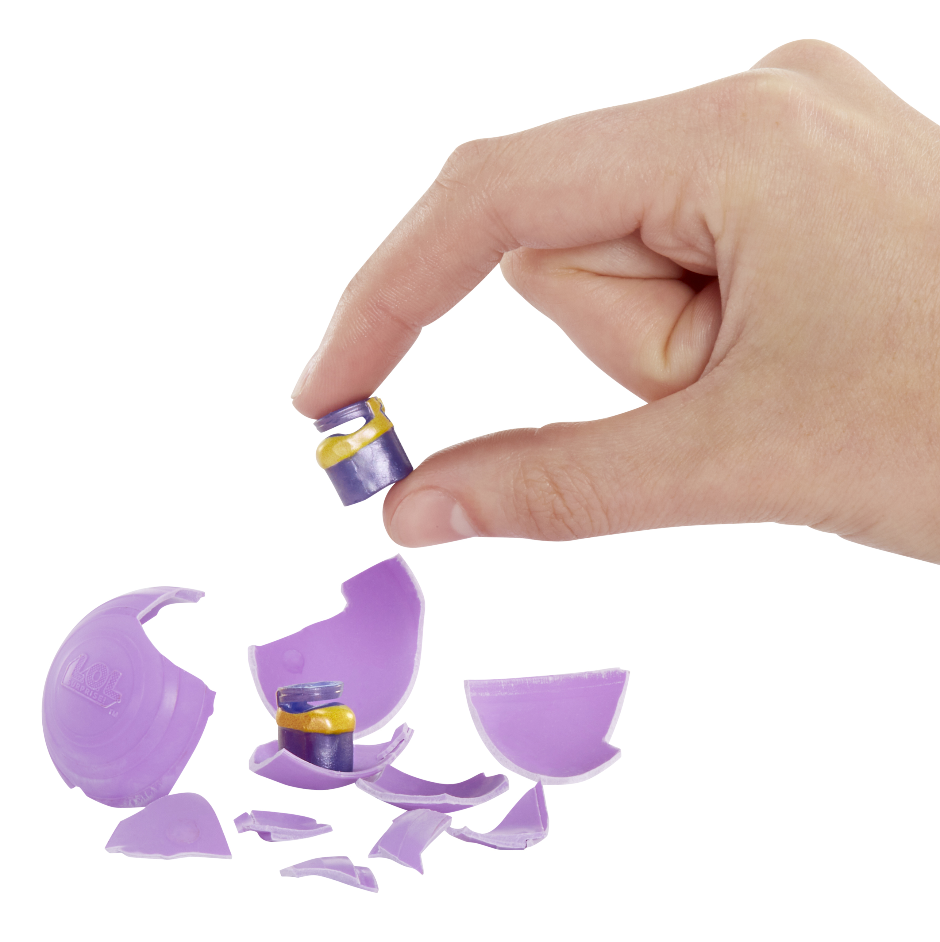 Dłoń trzyma miniaturową zabawkę. Rozbita fioletowa skorupka jajka na białym tle. Zabawka jest fioletowa i żółta.