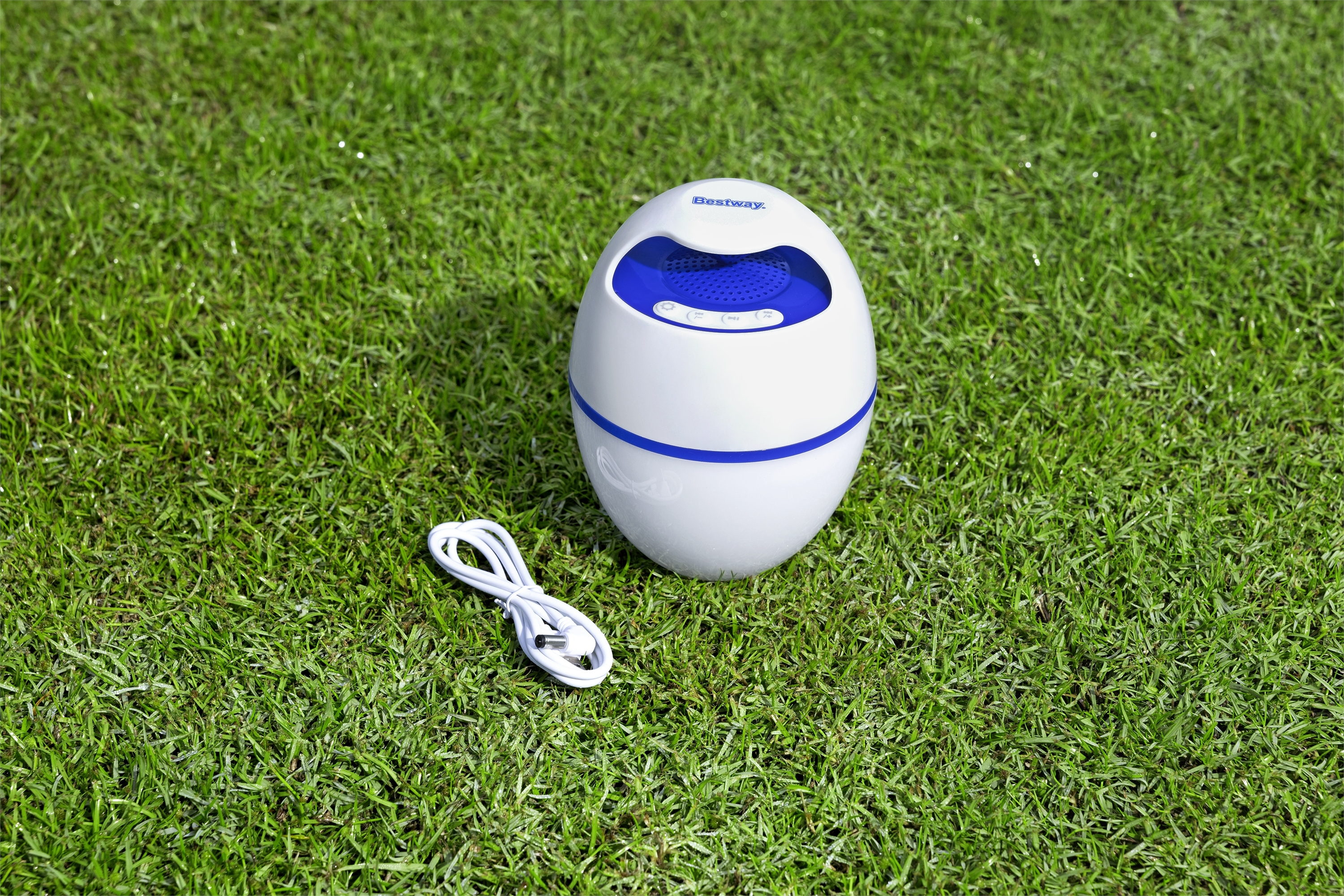 Biało-niebieski głośnik Bestway na zielonej trawie z białym kablem.