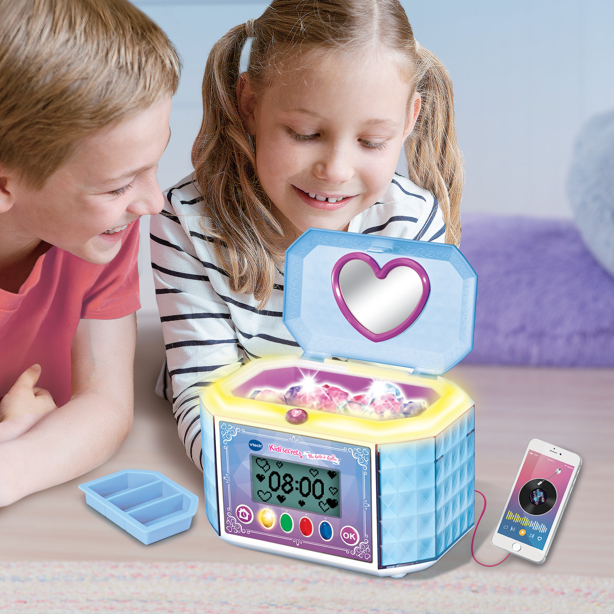 Zwei Kinder betrachten eine Schmuckschatulle. Die Schatulle ist blau mit einem Herzspiegel. Ein Telefon spielt Musik.