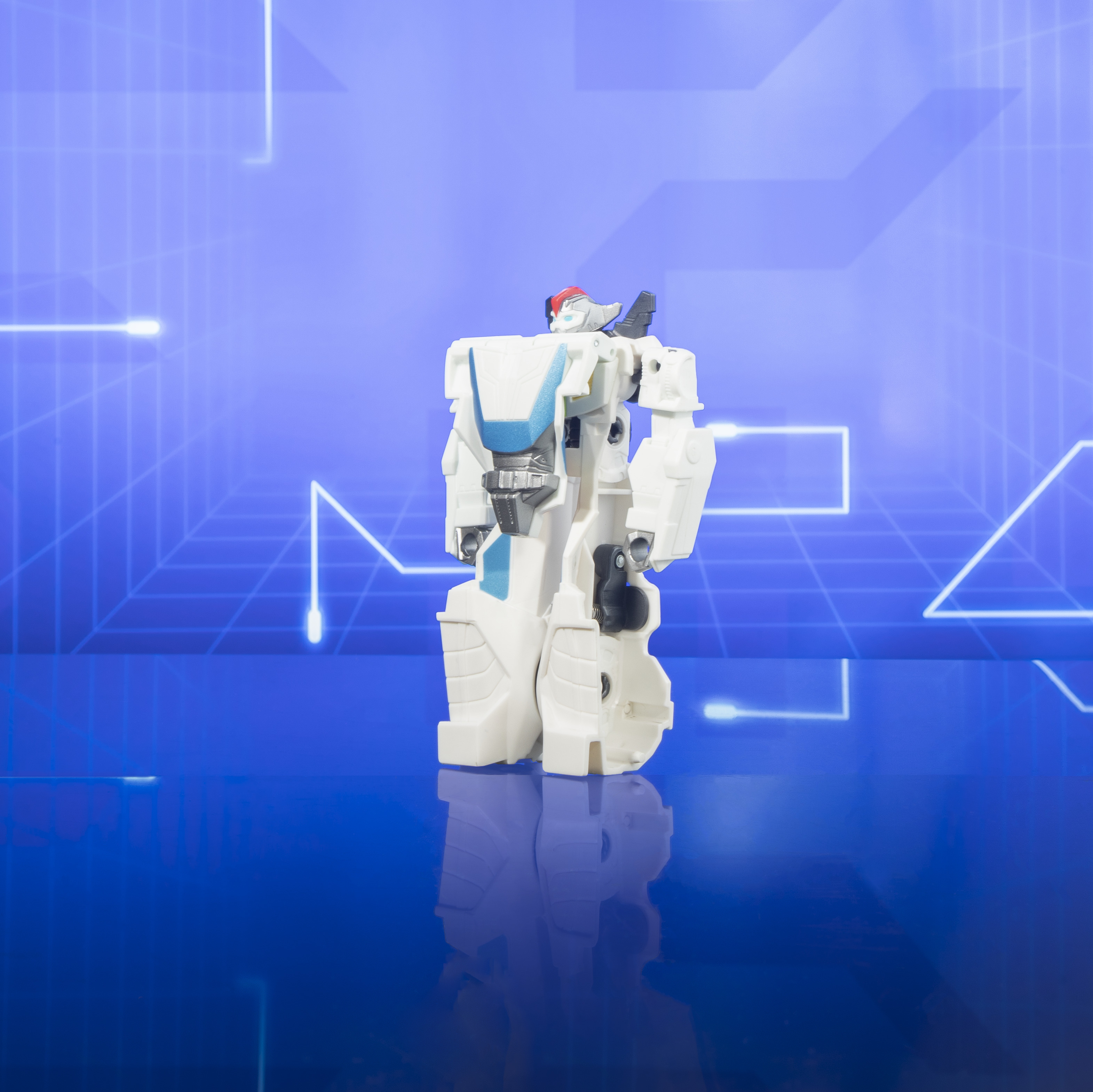 Biało-niebieska zabawka robota stoi na odblaskowej, niebieskiej powierzchni, na tle niebieskiego tła.