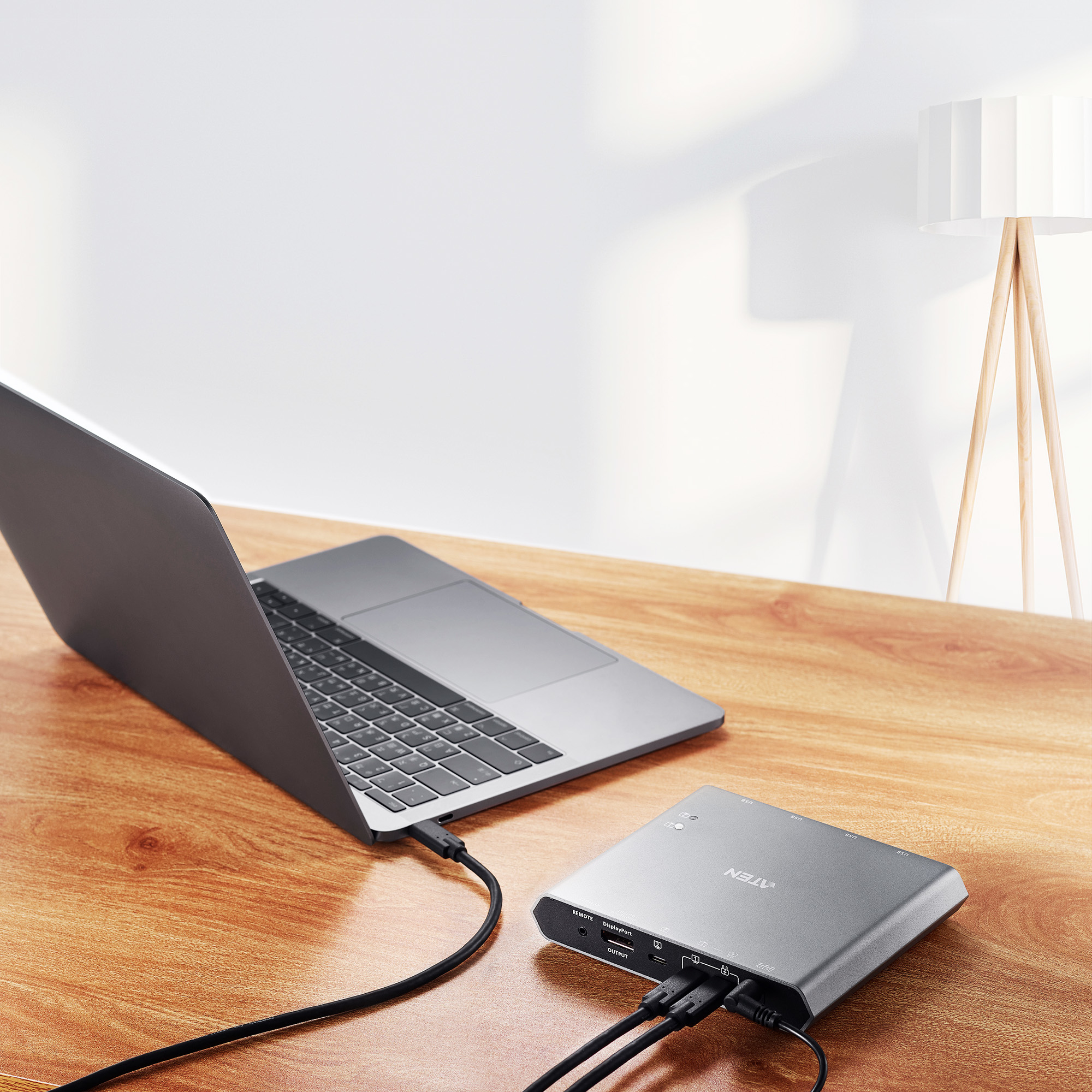 Ordinateur portable connecté à un appareil argenté sur un bureau en bois. Lampe en arrière-plan. Câbles connectés.