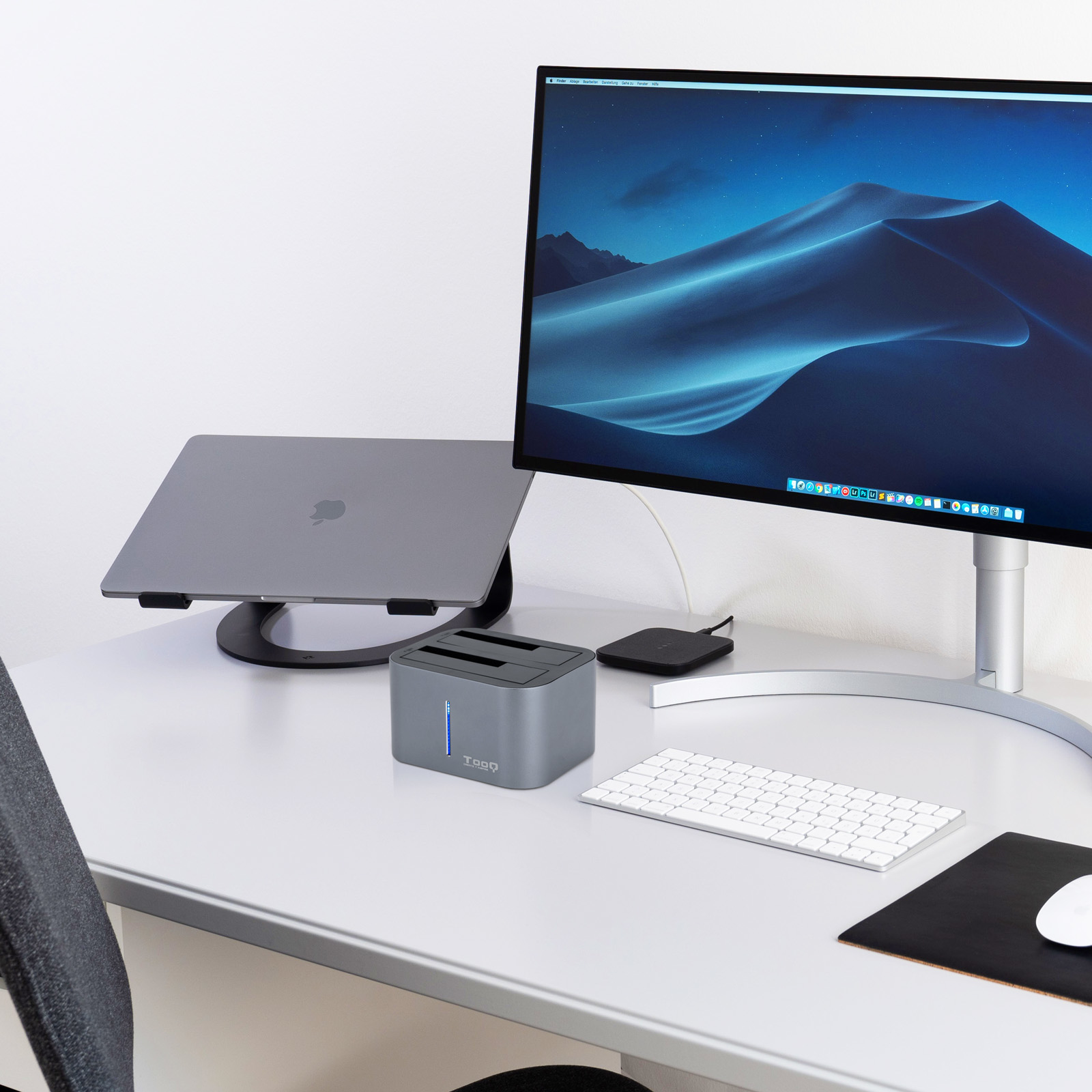 Escritorio con laptop, monitor, teclado y disco duro externo. El monitor muestra un paisaje desértico.