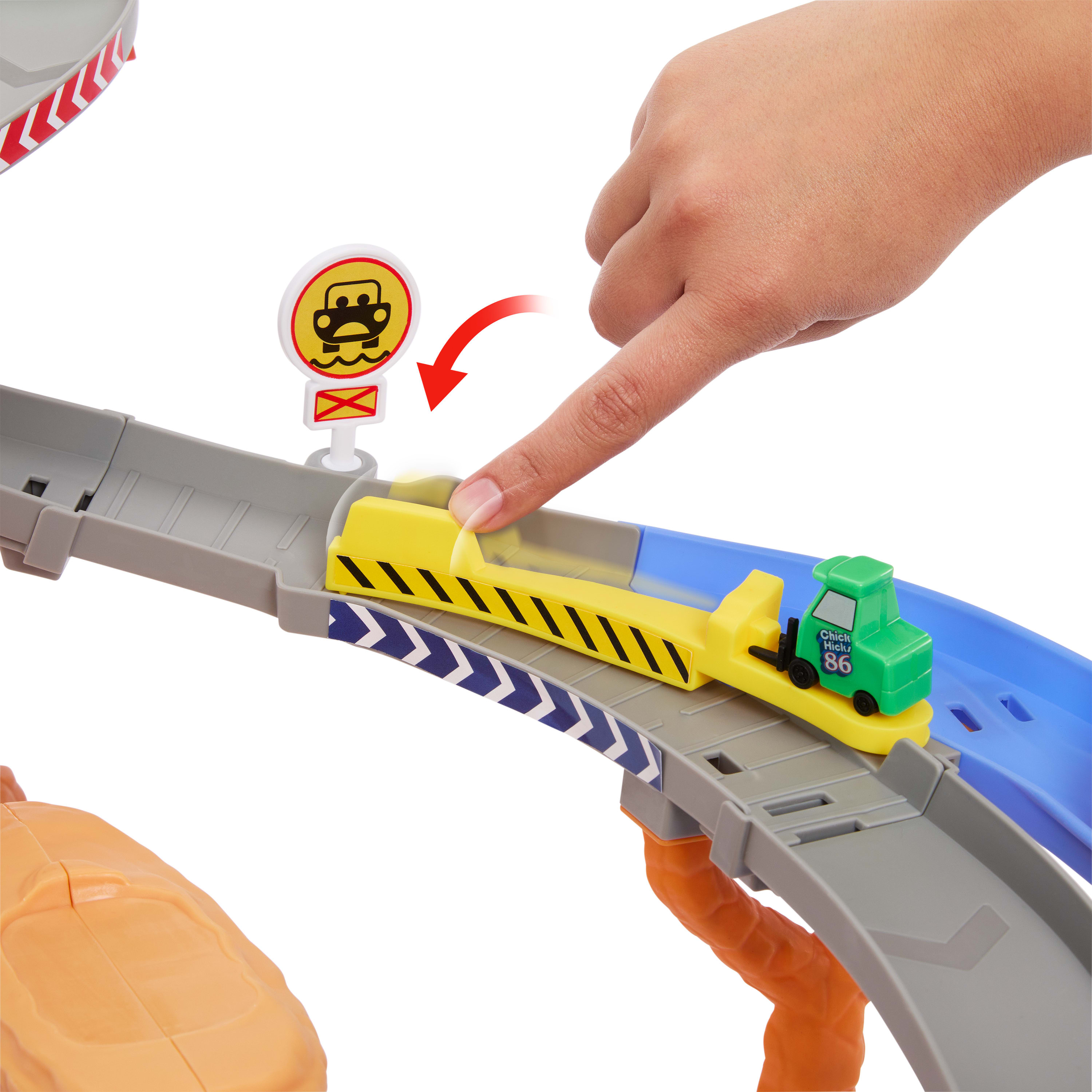 Ręka wskazuje na żółtą rampę ze znakiem i zielonym samochodzikiem. Rampa jest częścią toru wyścigowego.