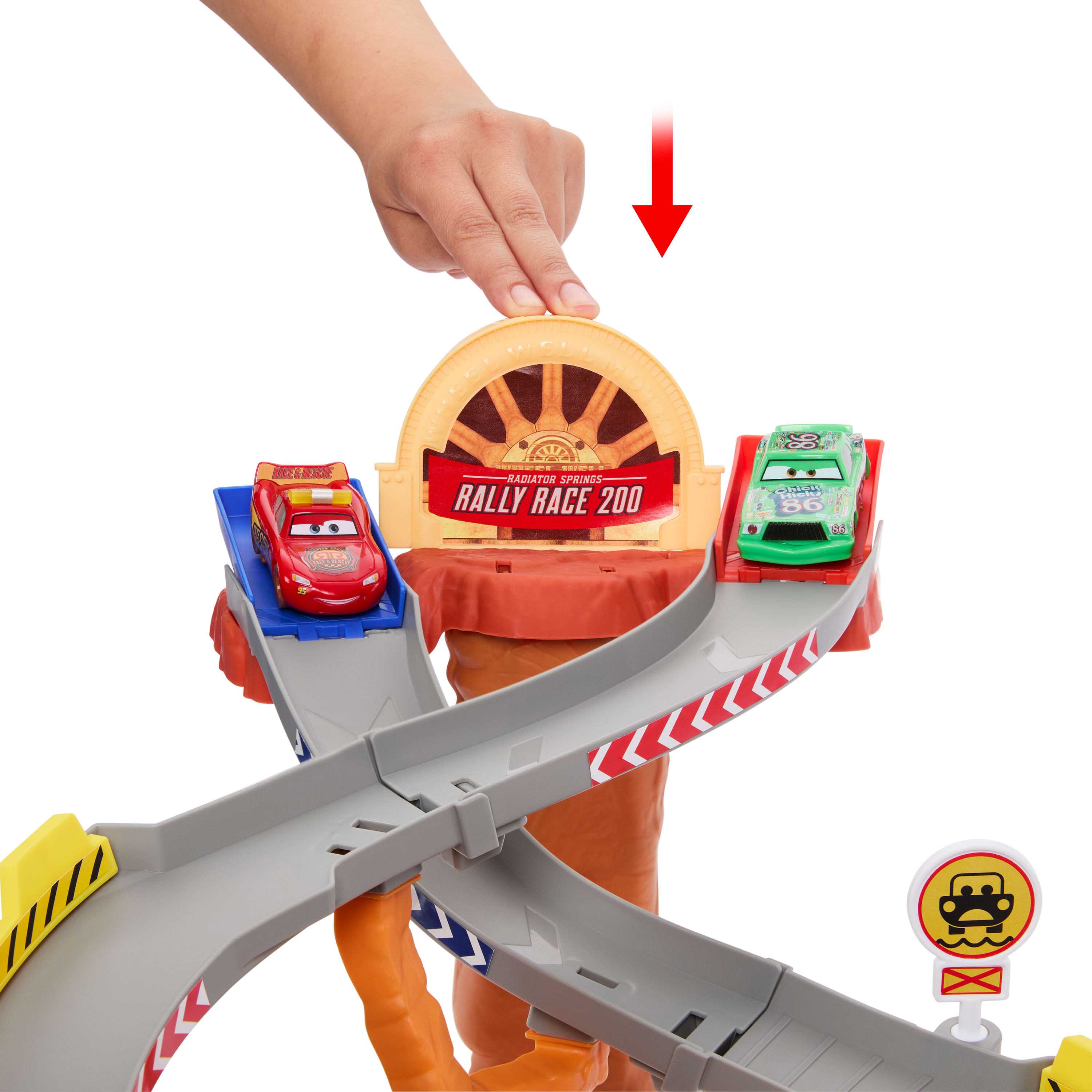 Ręka naciska dźwignię, aby wystrzelić zabawki samochodowe na tor wyścigowy. Czerwone i zielone samochody są na torze. Tło jest białe.
