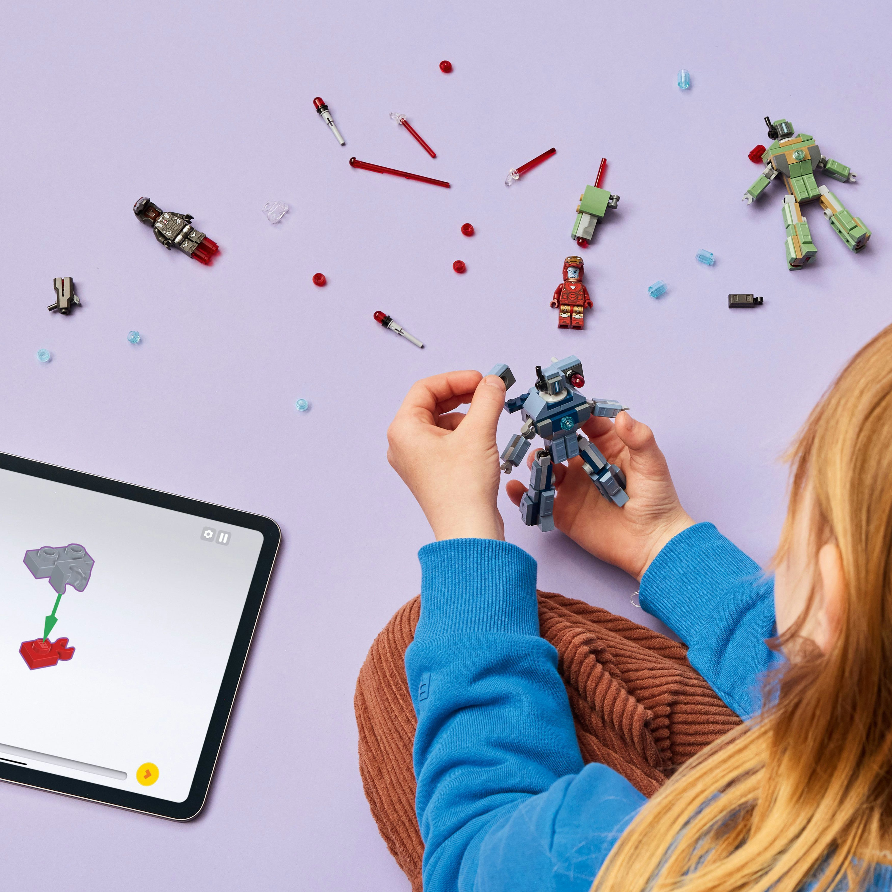 Un bambino assembla un robot giocattolo, pezzi sparsi su una superficie viola. Un iPad mostra le istruzioni.