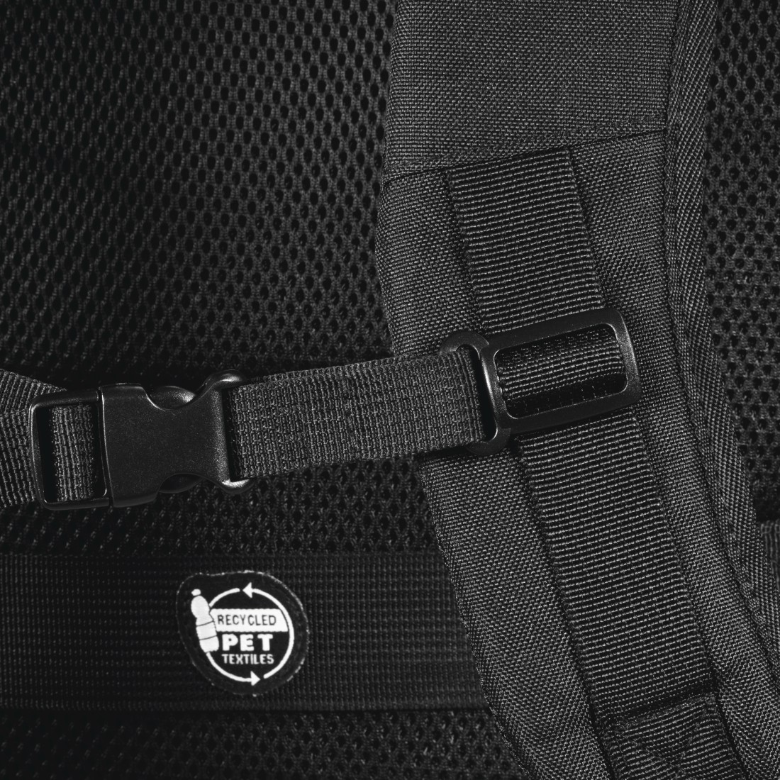 Zbliżenie czarnego plecaka z paskami, klamrami i etykietą z recyklingu PET. Tło to materiał siatkowy.