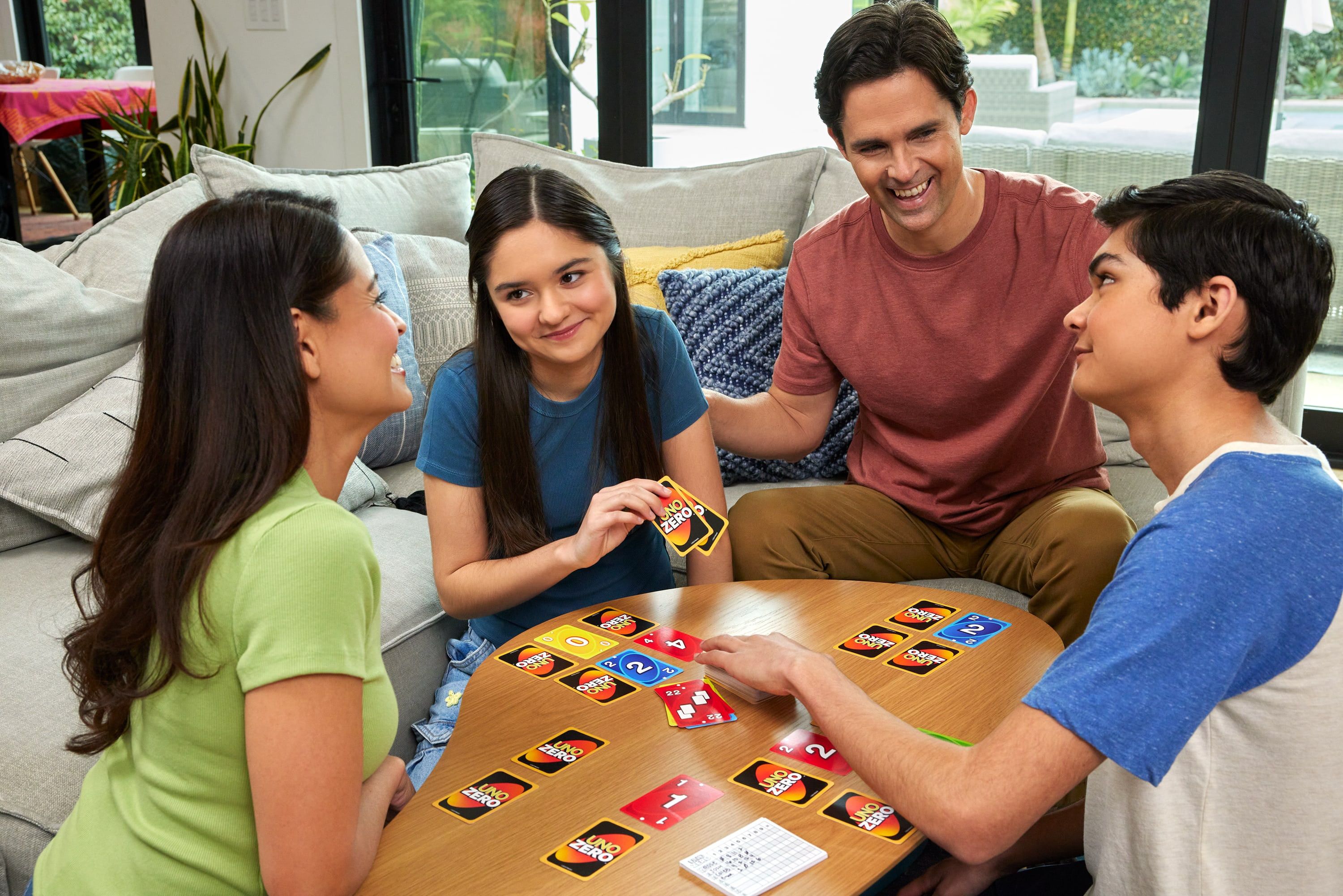 Famiglia che gioca a Uno Zero. Quattro persone sedute attorno a un tavolo con le carte. Un divano sullo sfondo.