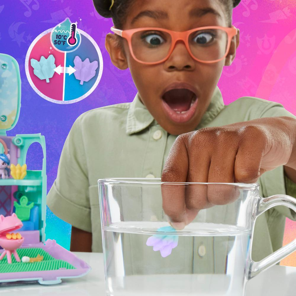 Una niña con gafas pone una flor de juguete en un vaso de agua, con expresión de sorpresa. Un juego de juguetes en el fondo.