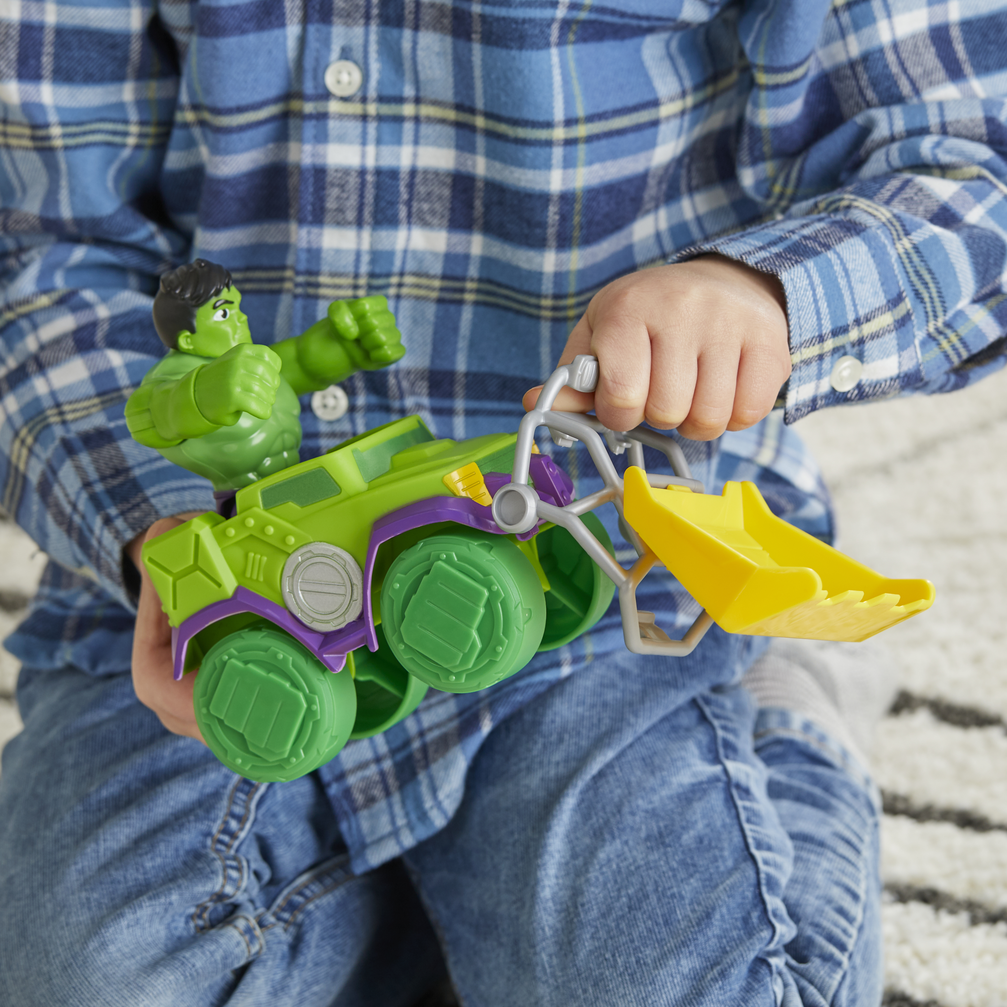 Ein Kind hält ein grünes Hulk-Spielzeug in einem Fahrzeug. Das Kind trägt Jeans und ein kariertes Hemd. Der Hintergrund ist ein Teppich.