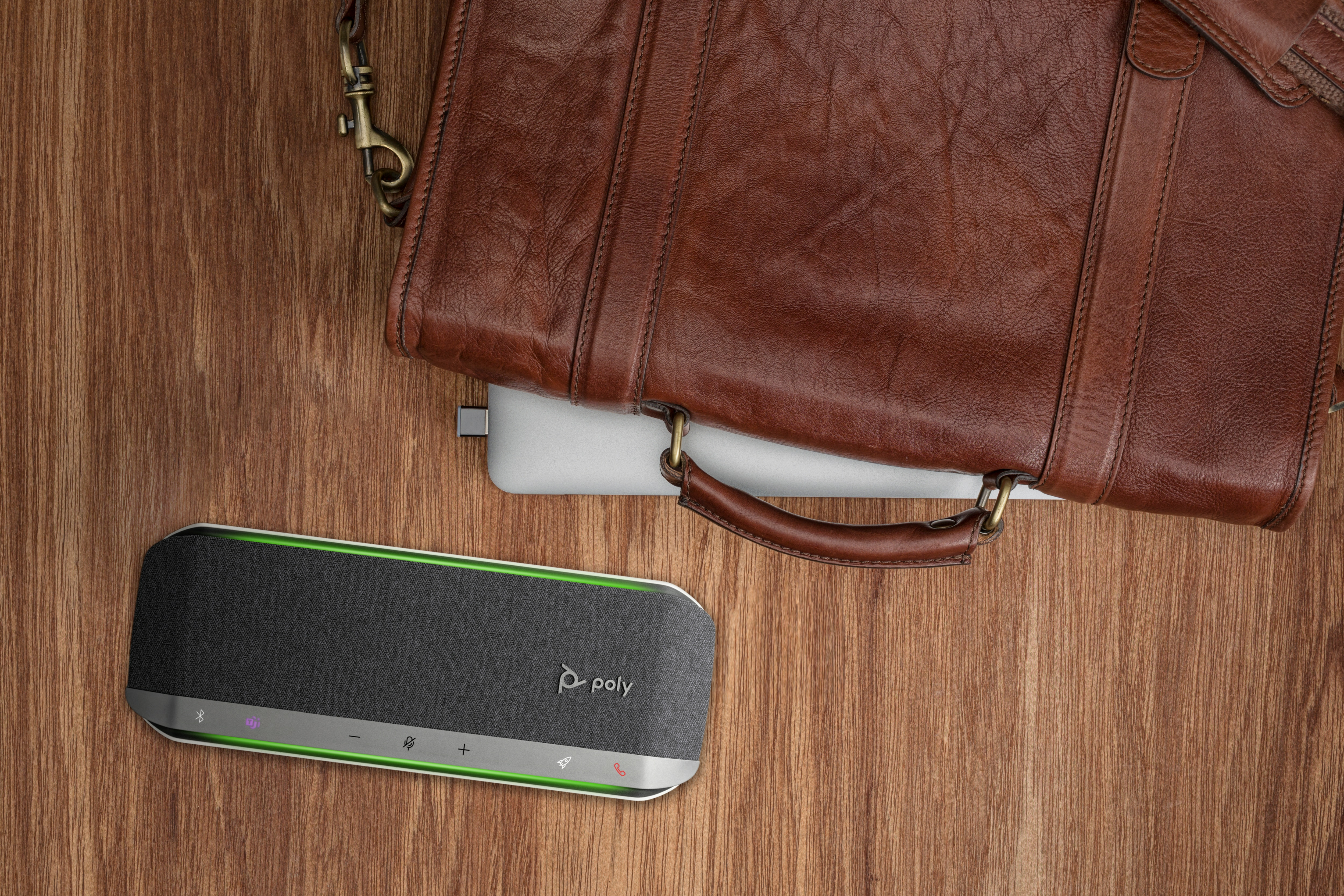 Vista superior: altavoz, bolso de cuero marrón y portátil sobre una superficie de madera.