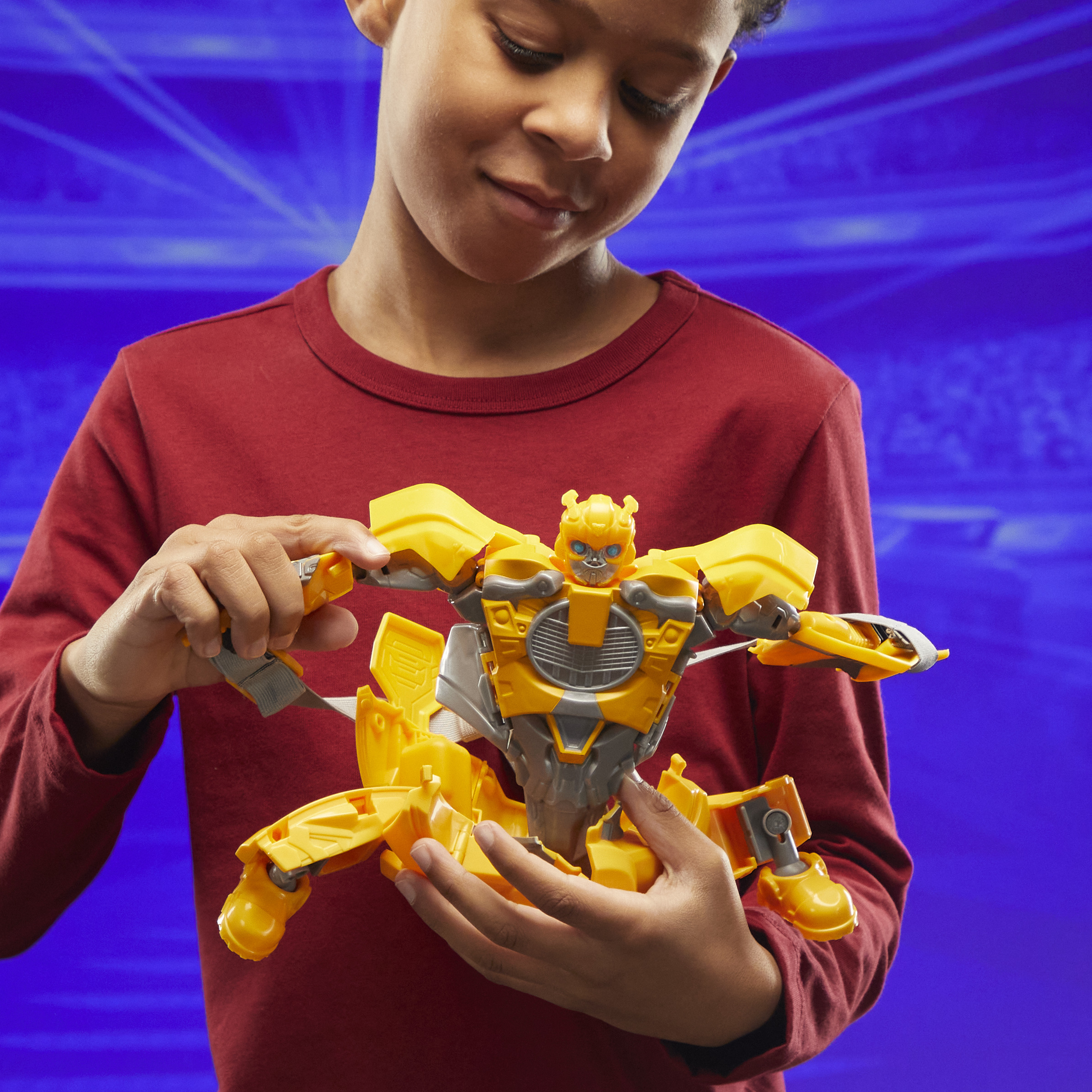 Un niño sostiene un juguete amarillo de Bumblebee. Lleva una camisa roja. El fondo es un degradado azul.