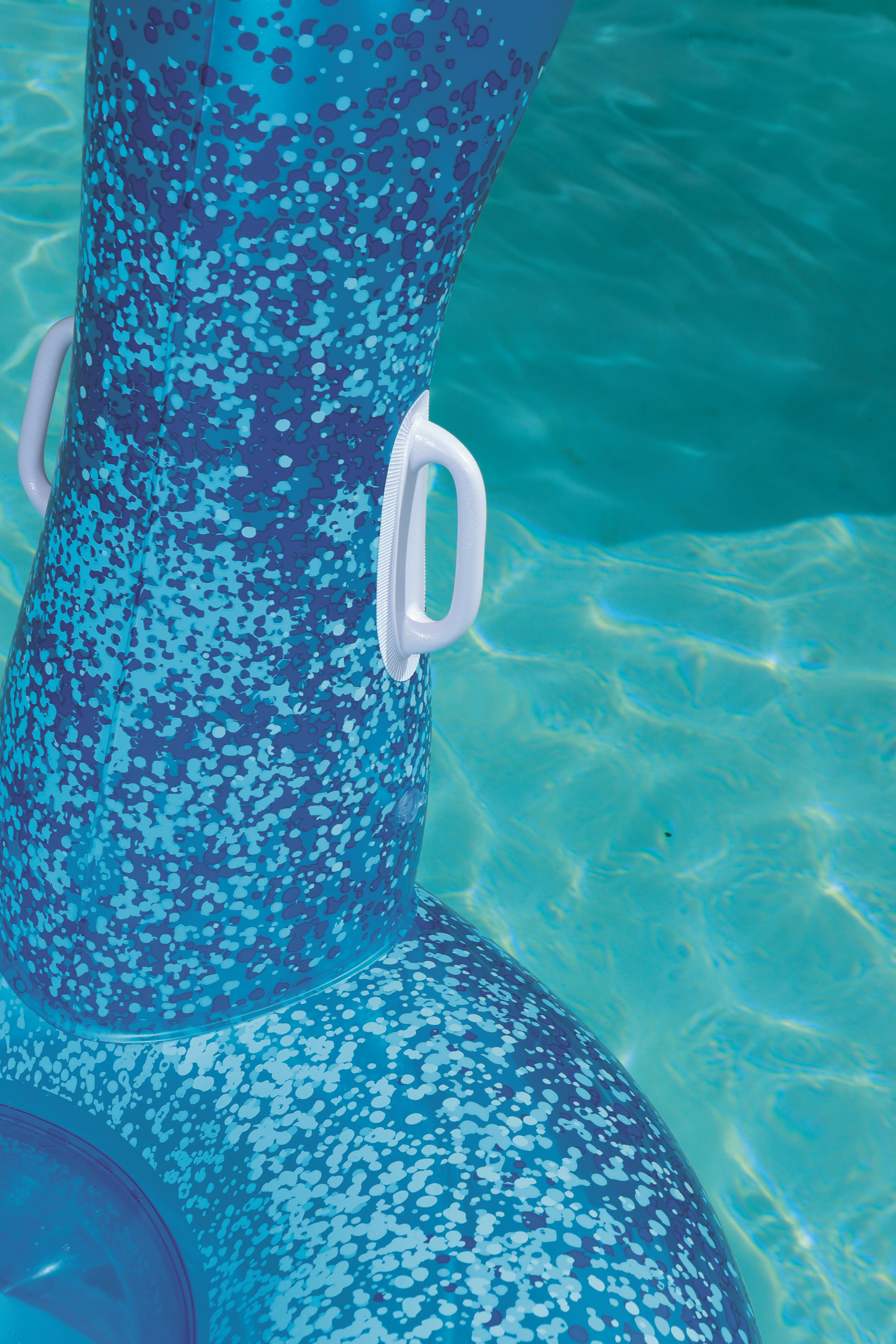 Ein blaues aufblasbares Pool-Schwimmgerät mit weißen Griffen schwimmt auf türkisfarbenem Wasser. Das Schwimmgerät hat ein Muster aus blauen und weißen Punkten.